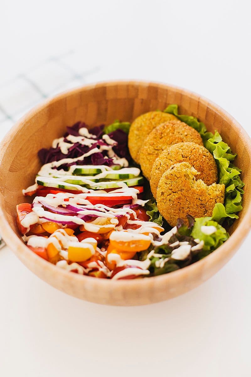 Side view of salad bowl with falafels and tahini drizzle.