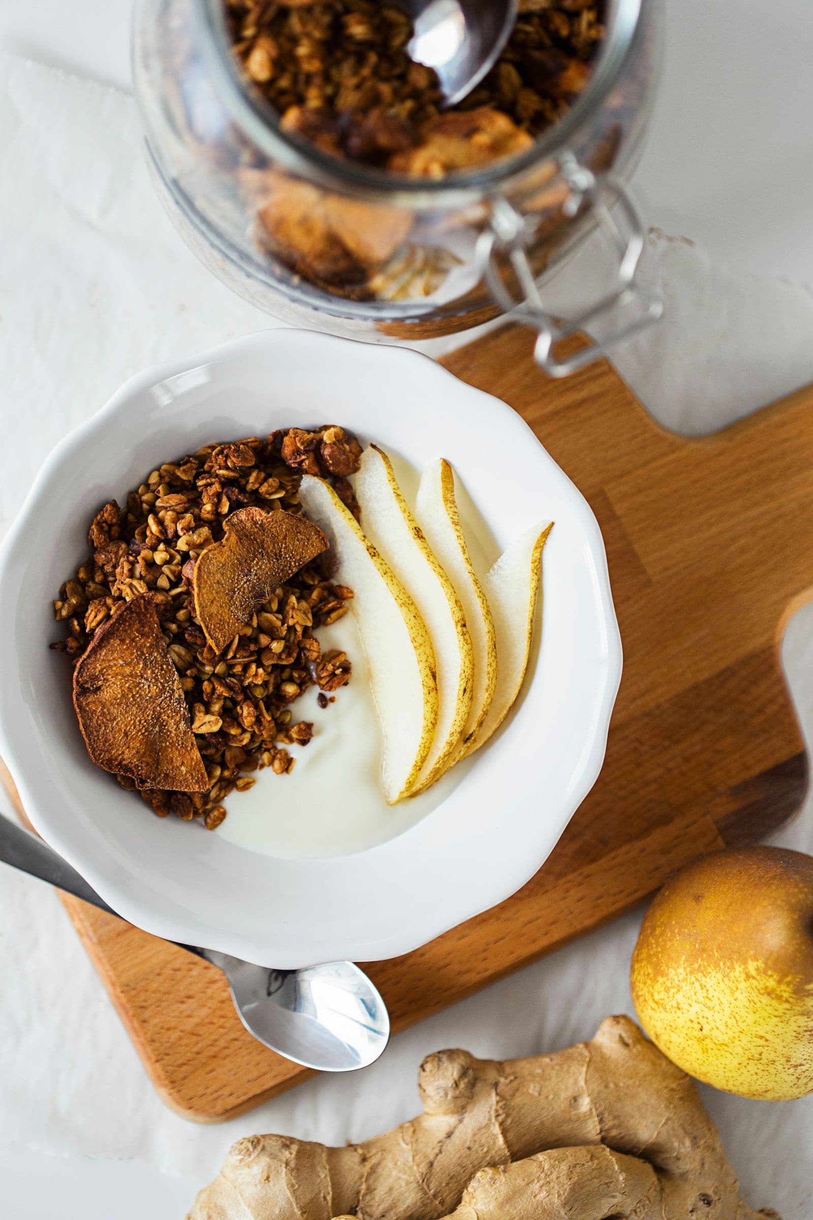 Bowl of yogurt topped with pear & ginger granola and sliced pear.