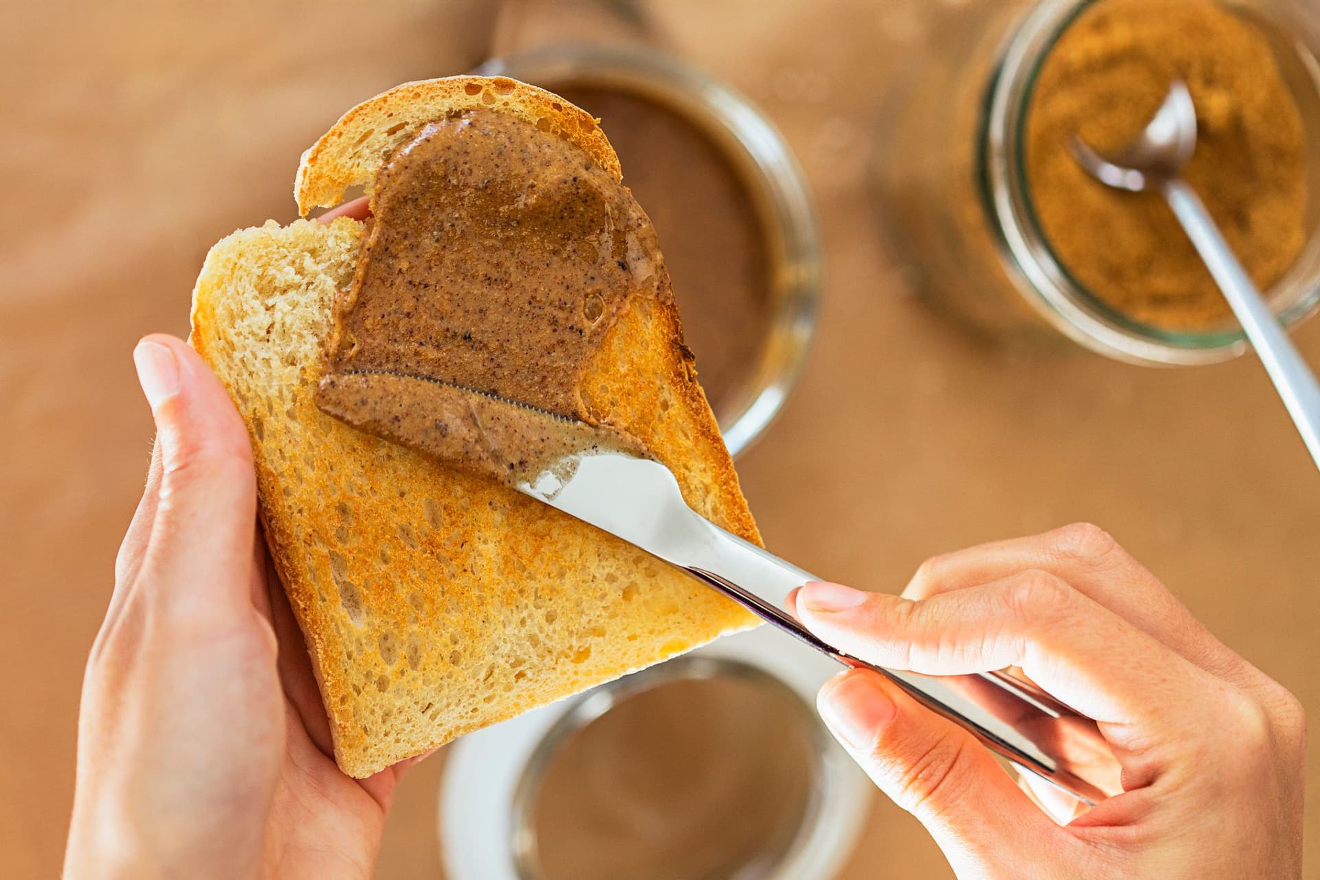 Hands spreading almond butter onto a slice of toast.