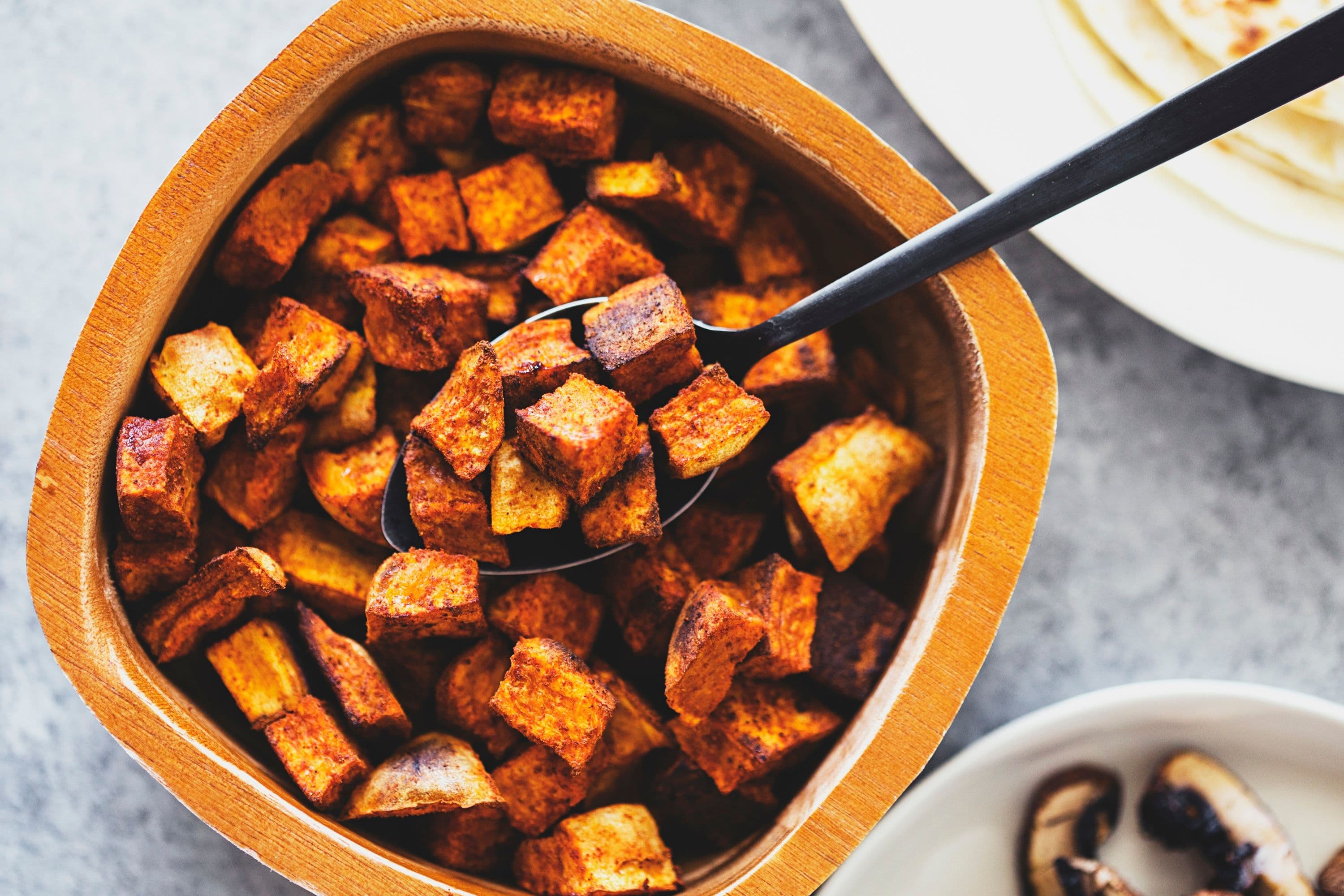 Bowl filled with roasted sweet potato cubes, spoon inside.