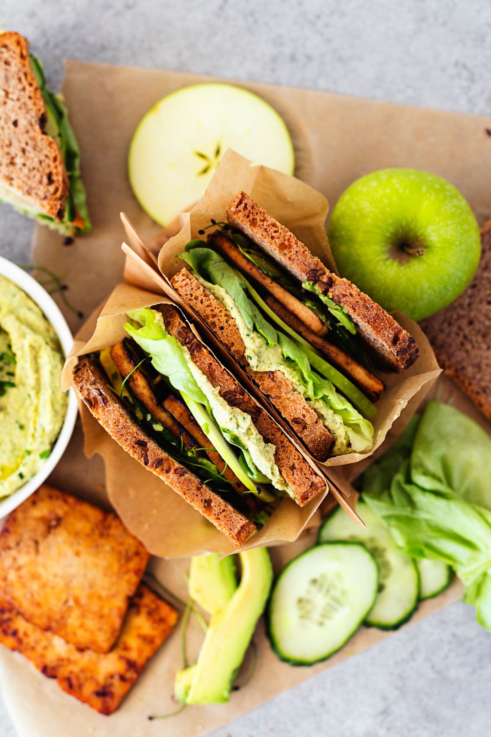Flat lay of assembled sandwich with green apple, cucumber, tofu and hummus.