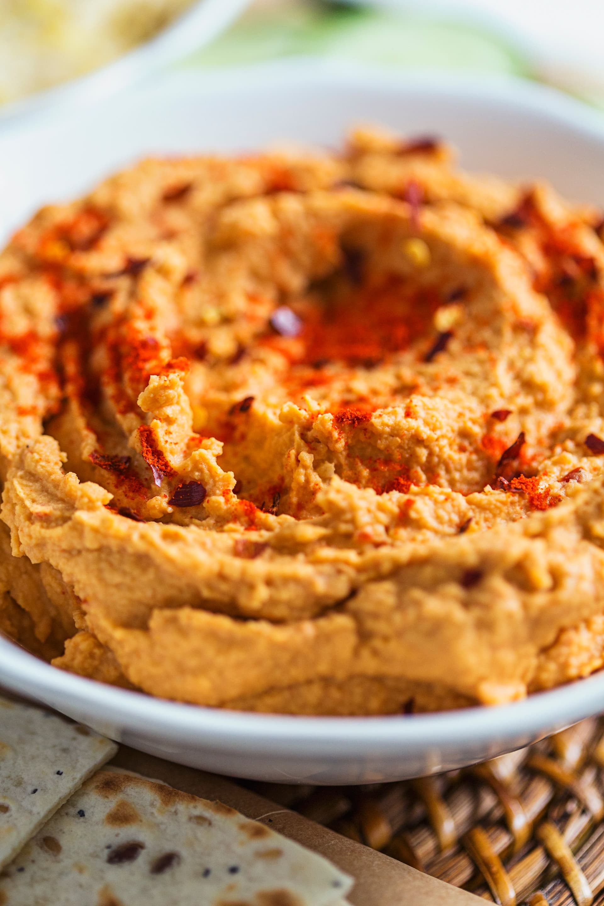 Close-up of creamy tomato hummus in a white bowl, topped with smoked paprika and olive oil.