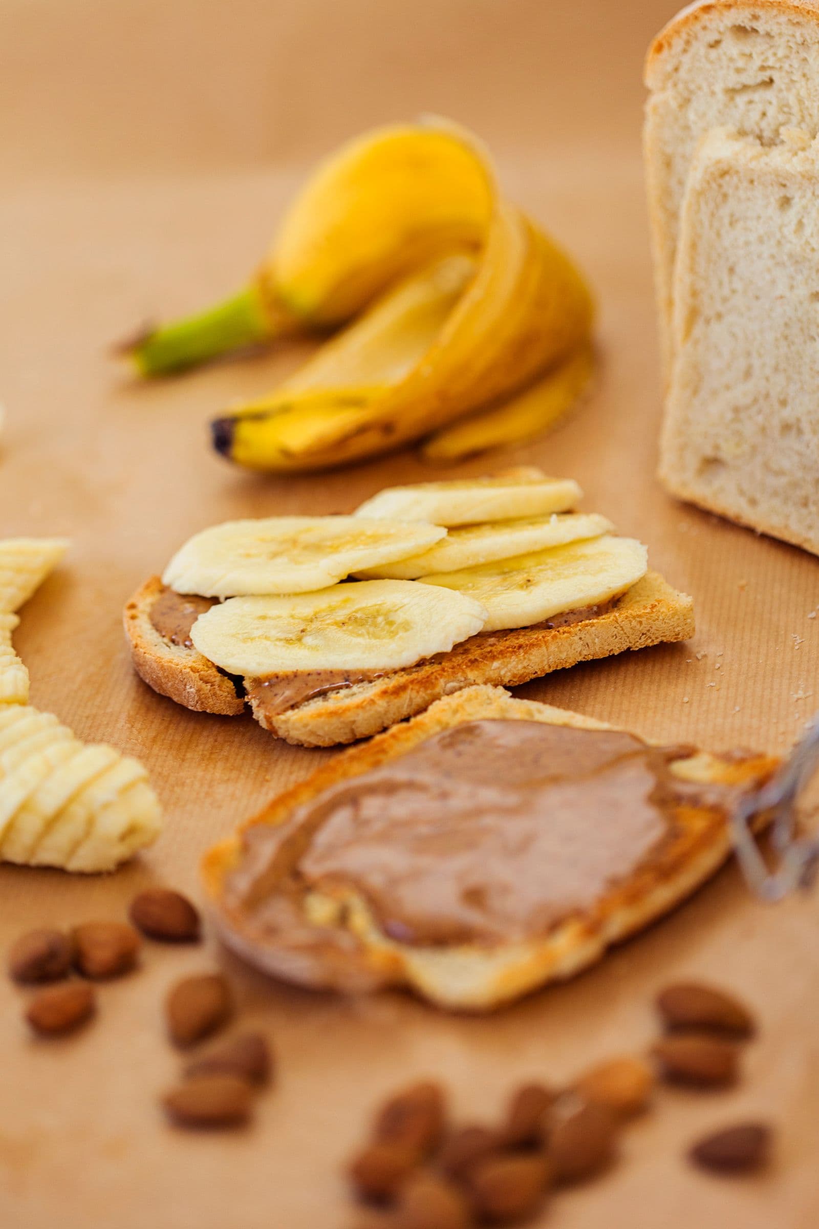 Ingredientes dispostos com uma tosta já preparada: banana, pão, manteiga de amêndoa e amêndoas.