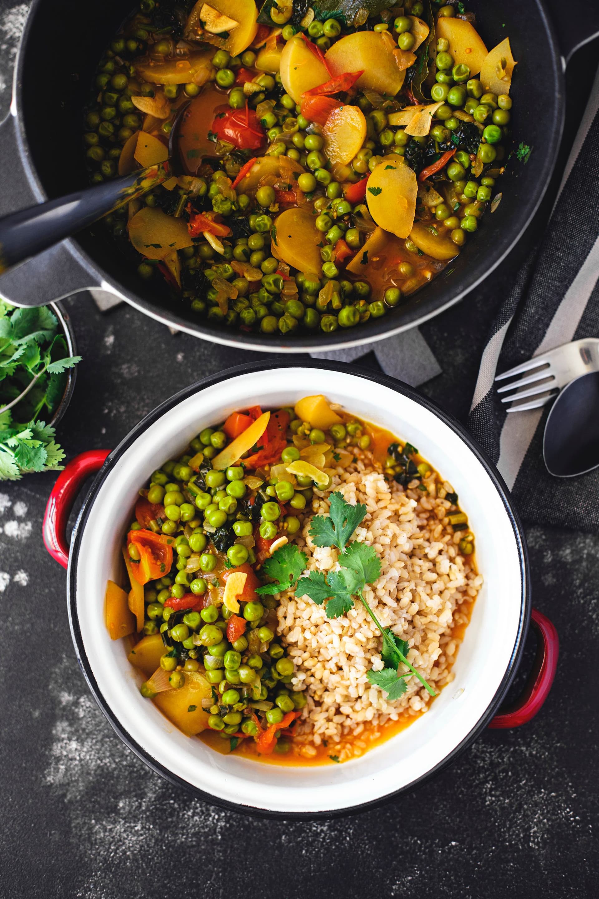 Overhead shot of a bowl filled with pea stew and a pot with rice and stew, on a striped tablecloth.