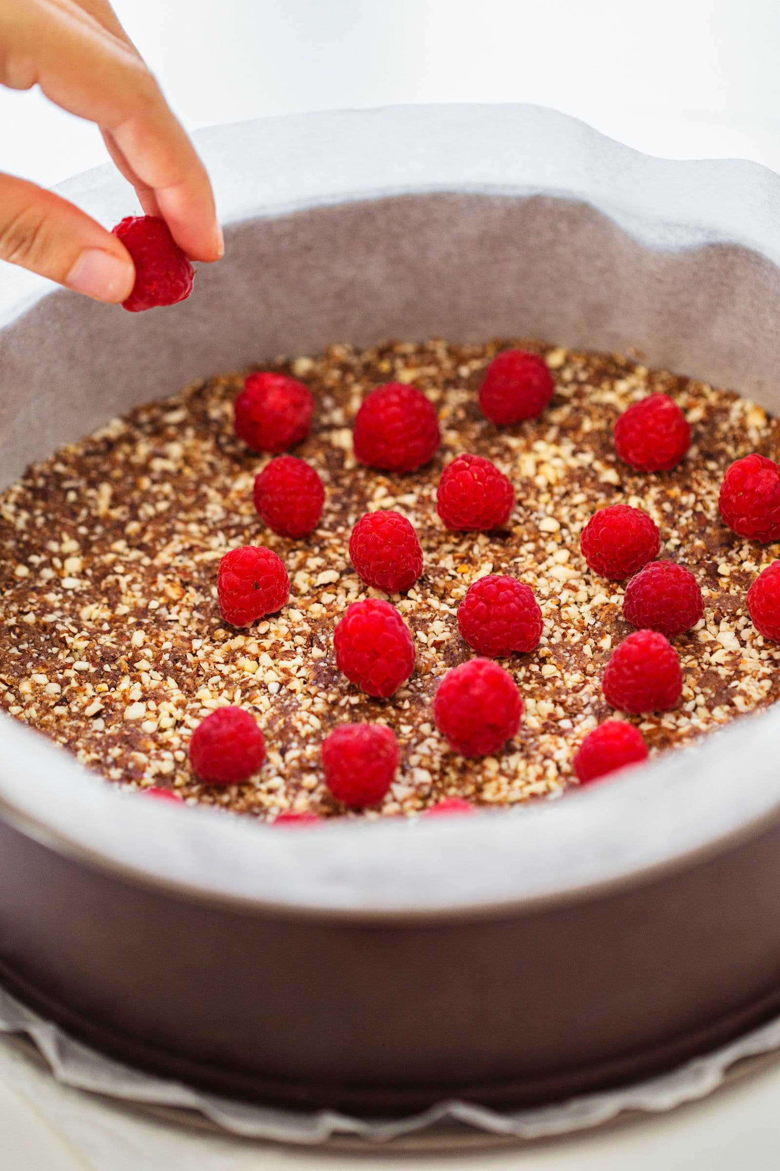 Hand placing fresh raspberries onto the pressed crust.