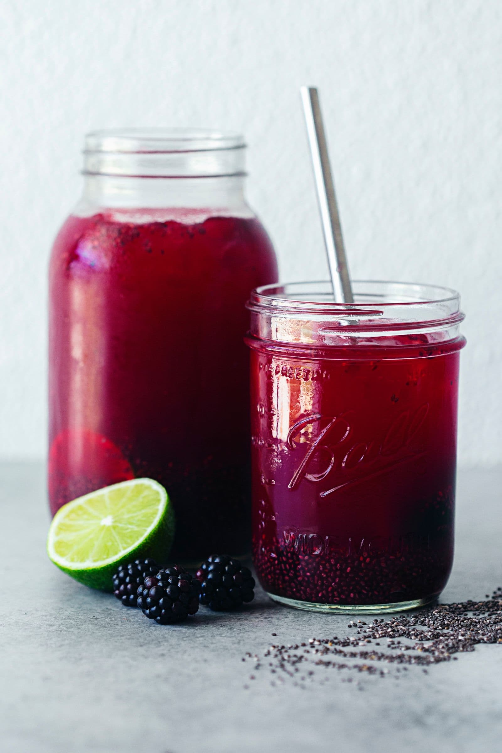 Copo pequeno e frasco grande com chia fresca, lima, amoras e sementes espalhadas.