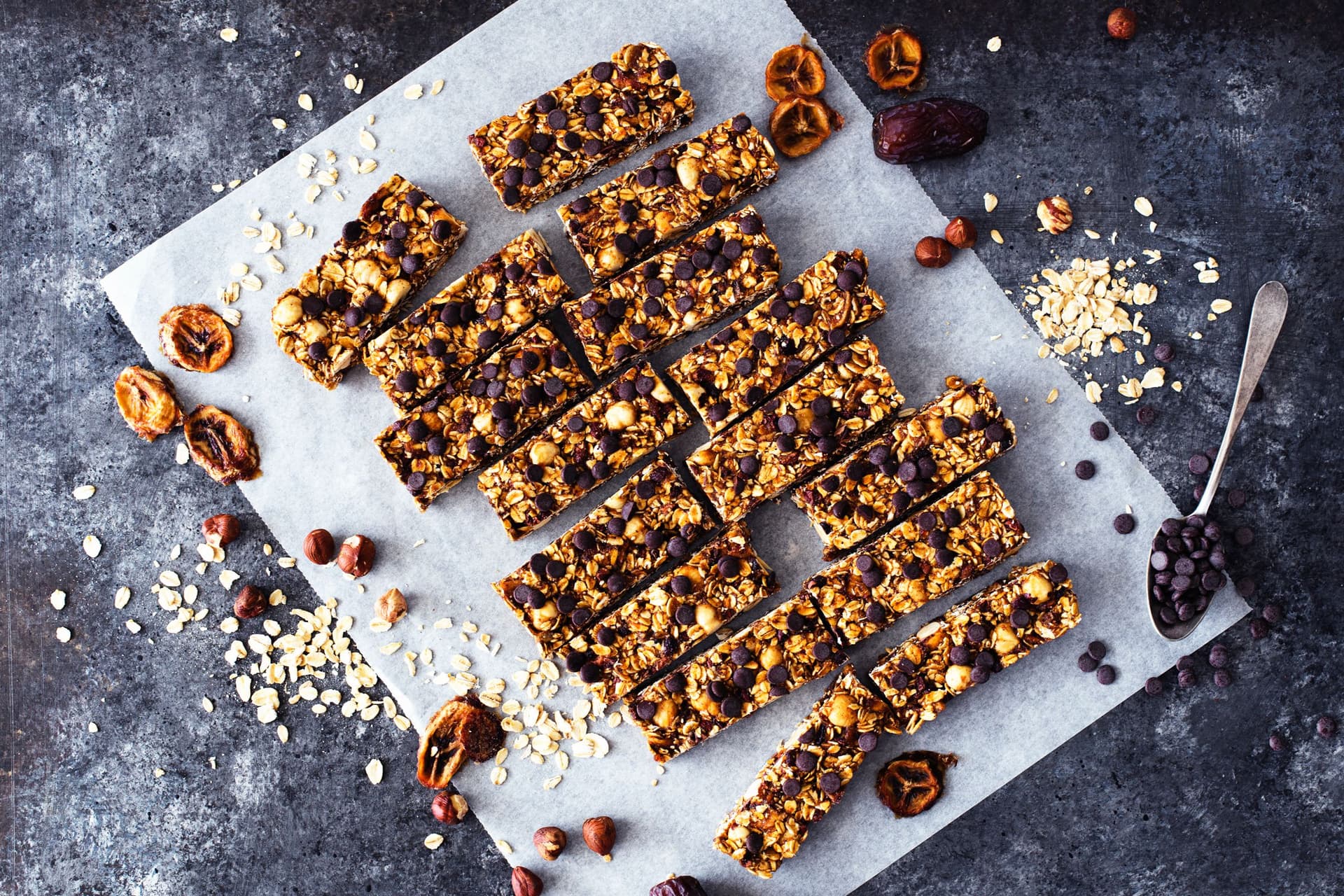 Cut granola bars on parchment with scattered ingredients, shown from above.