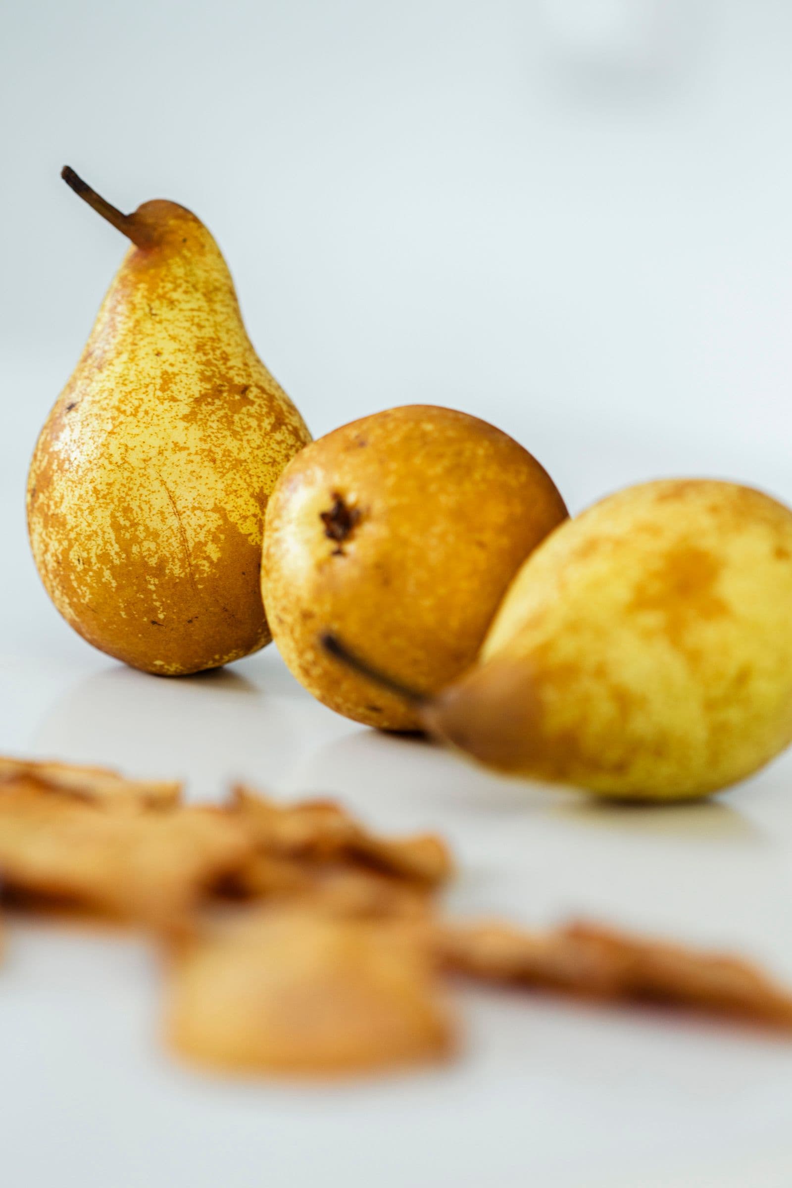 Three fresh yellow pears on a white surface.