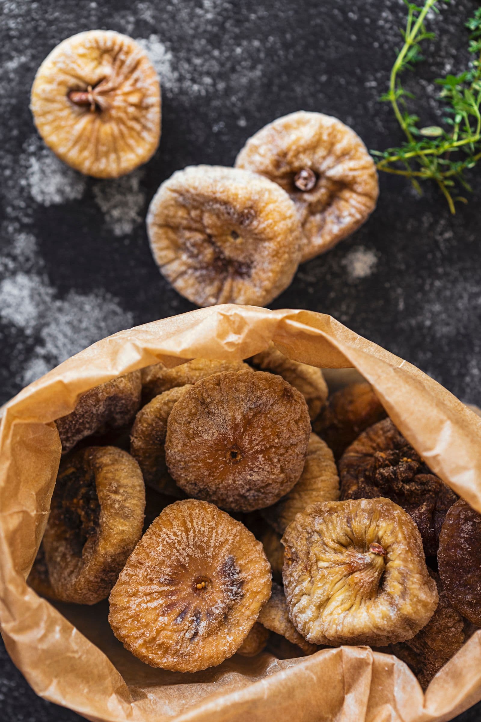 Paper bag filled with dried figs next to fresh thyme.