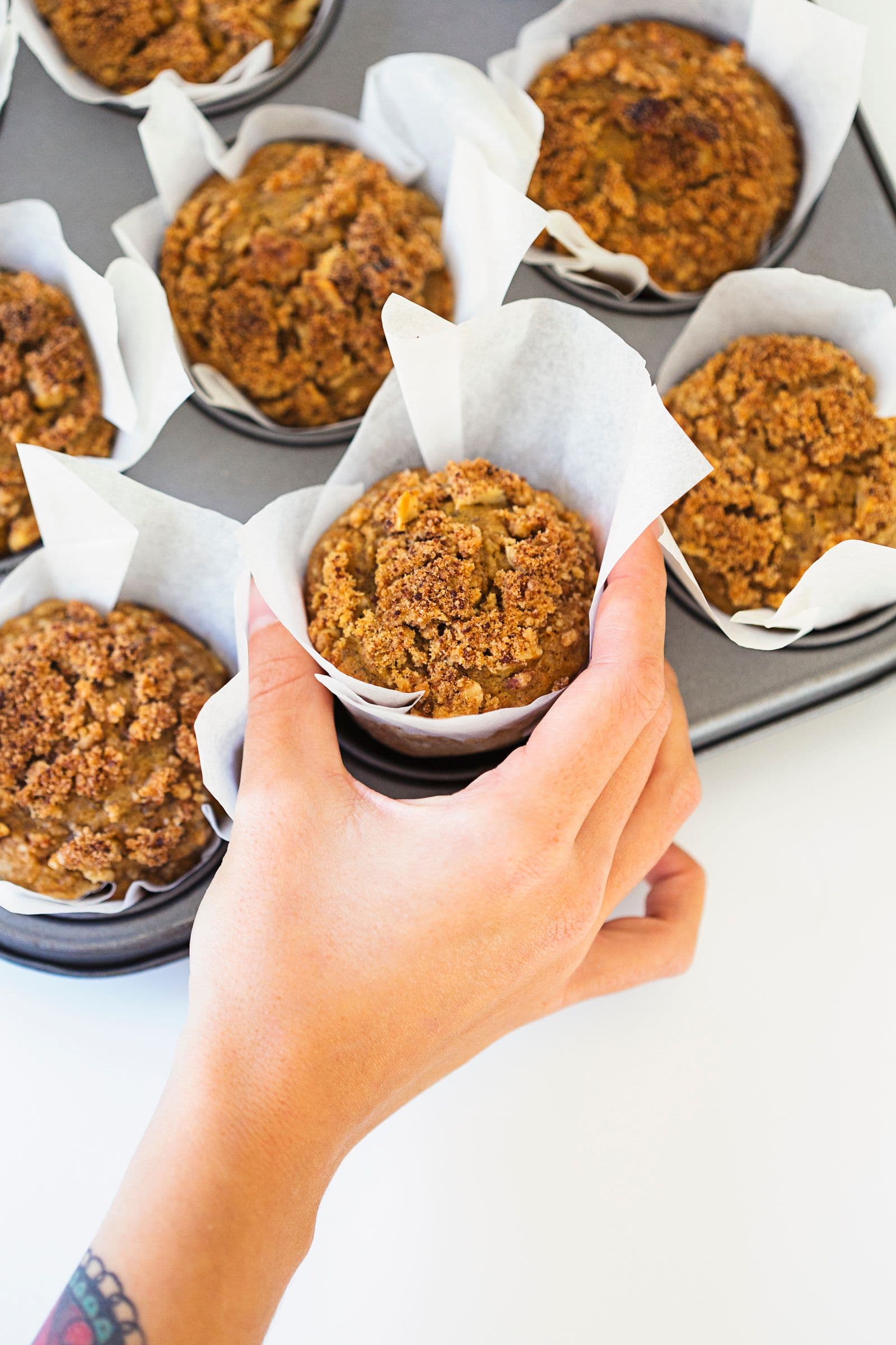 Person removing a single muffin from the tray.
