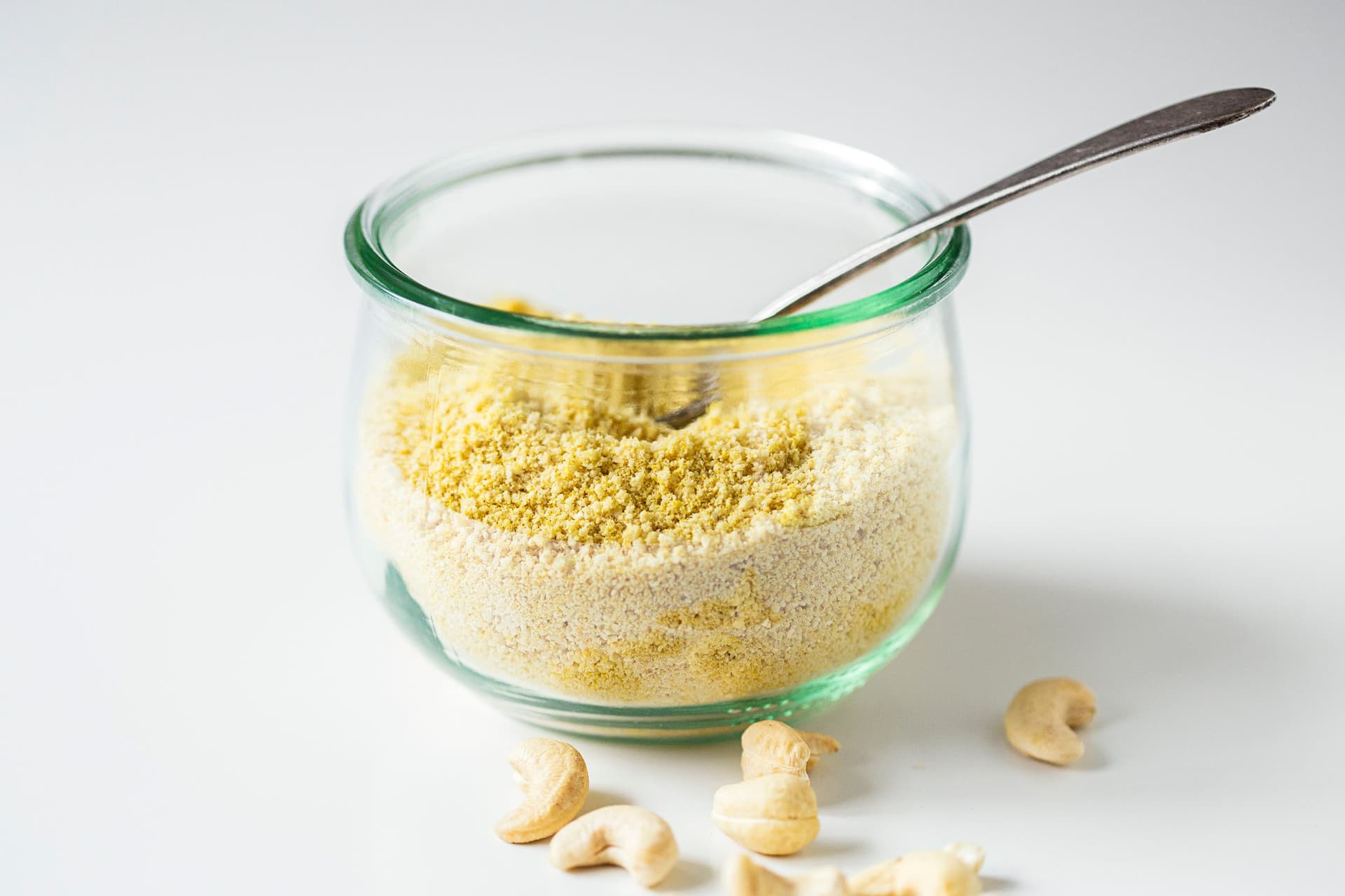 Glass jar filled with vegan parmesan cheese with a spoon inside.