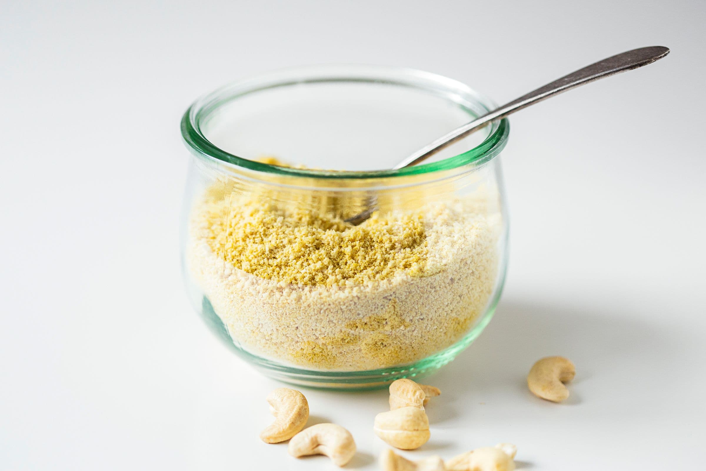 Glass jar filled with vegan parmesan cheese with a spoon inside.
