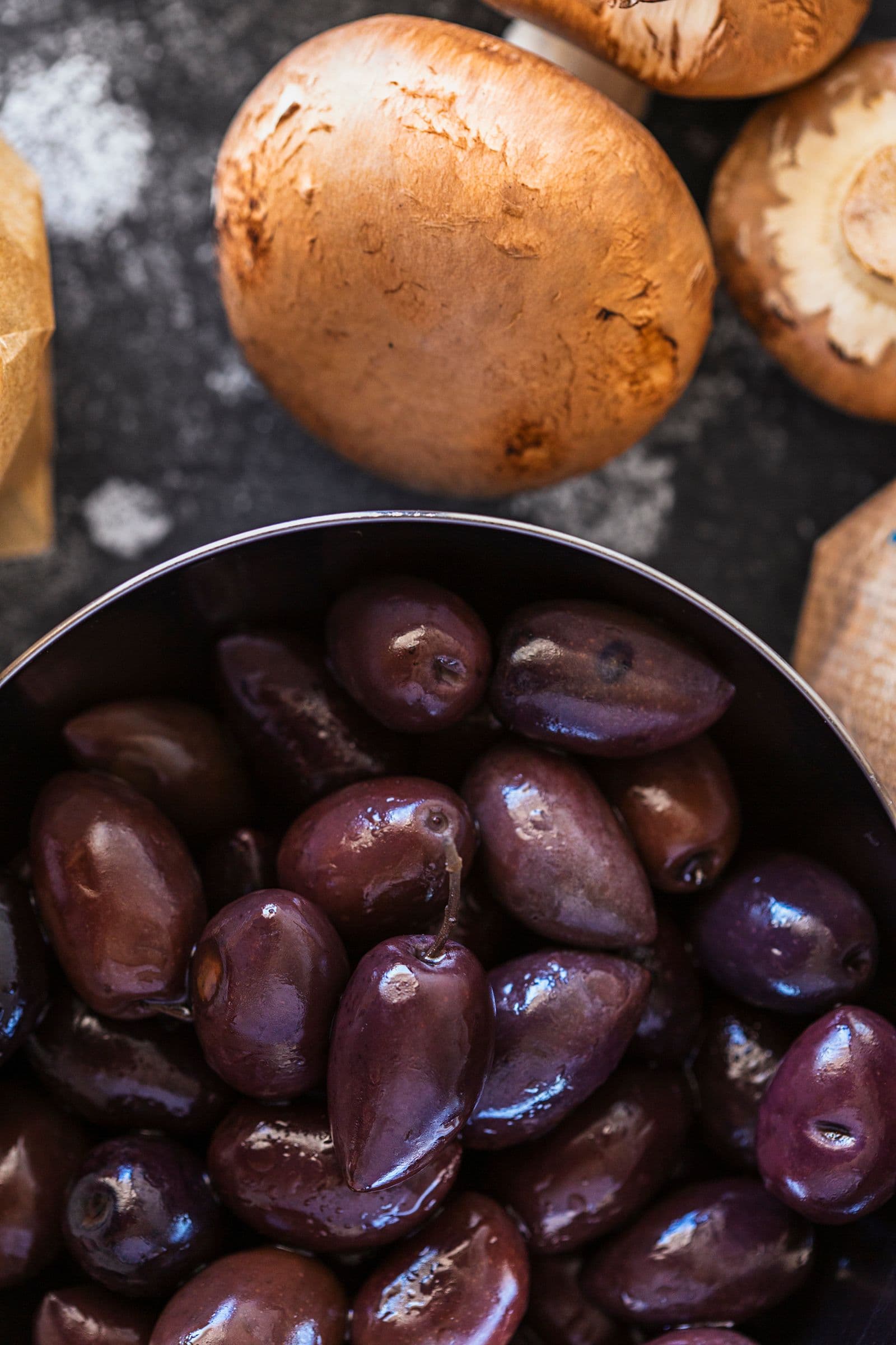 Black Kalamata olives in a small bowl beside mushrooms.