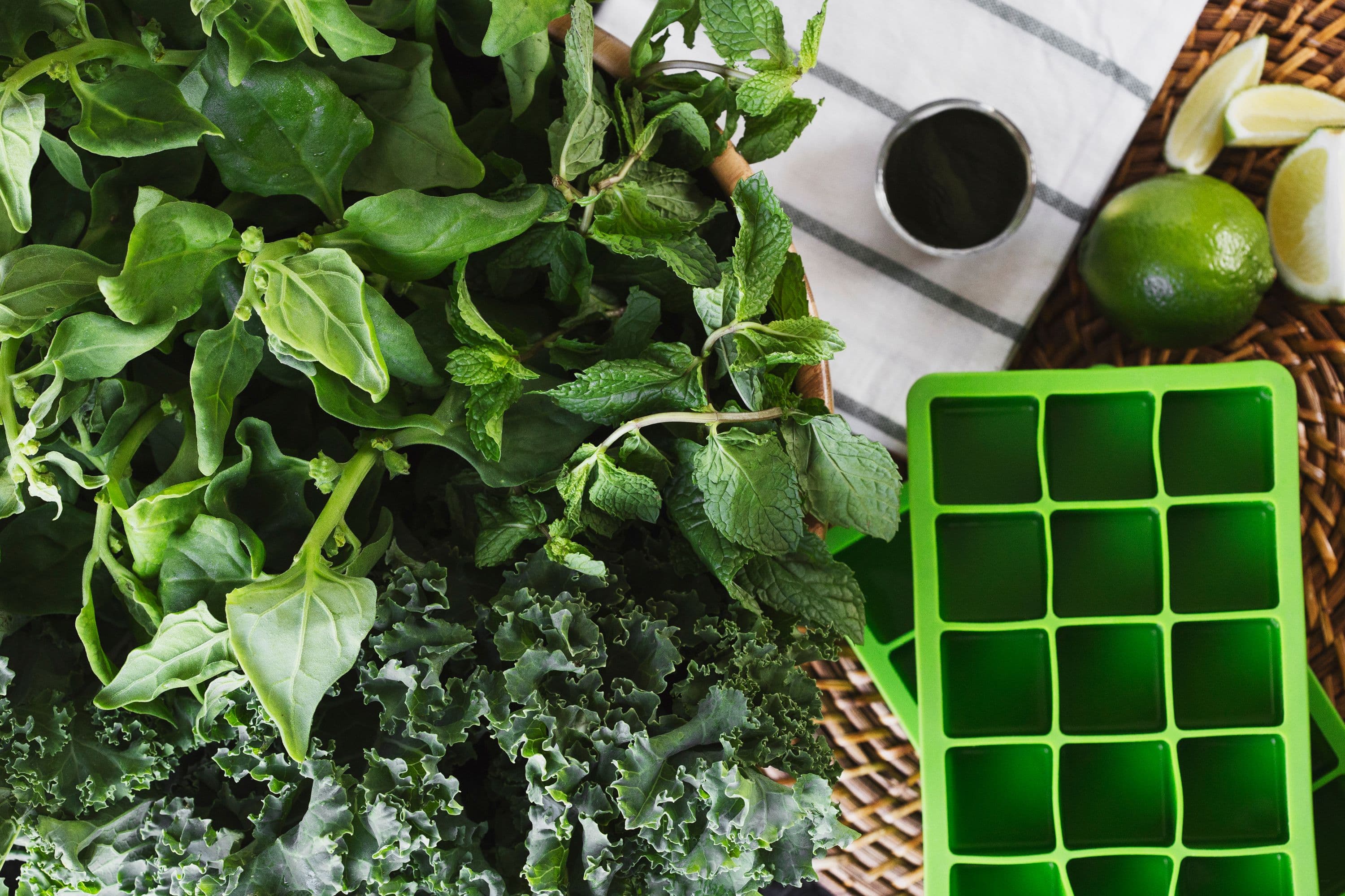 Fresh leafy greens, limes, and a green ice cube tray laid out on a table.