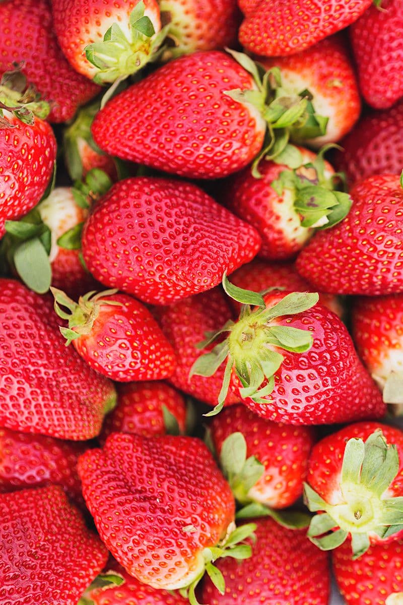 Close-up of a pile of fresh red strawberries with green tops.