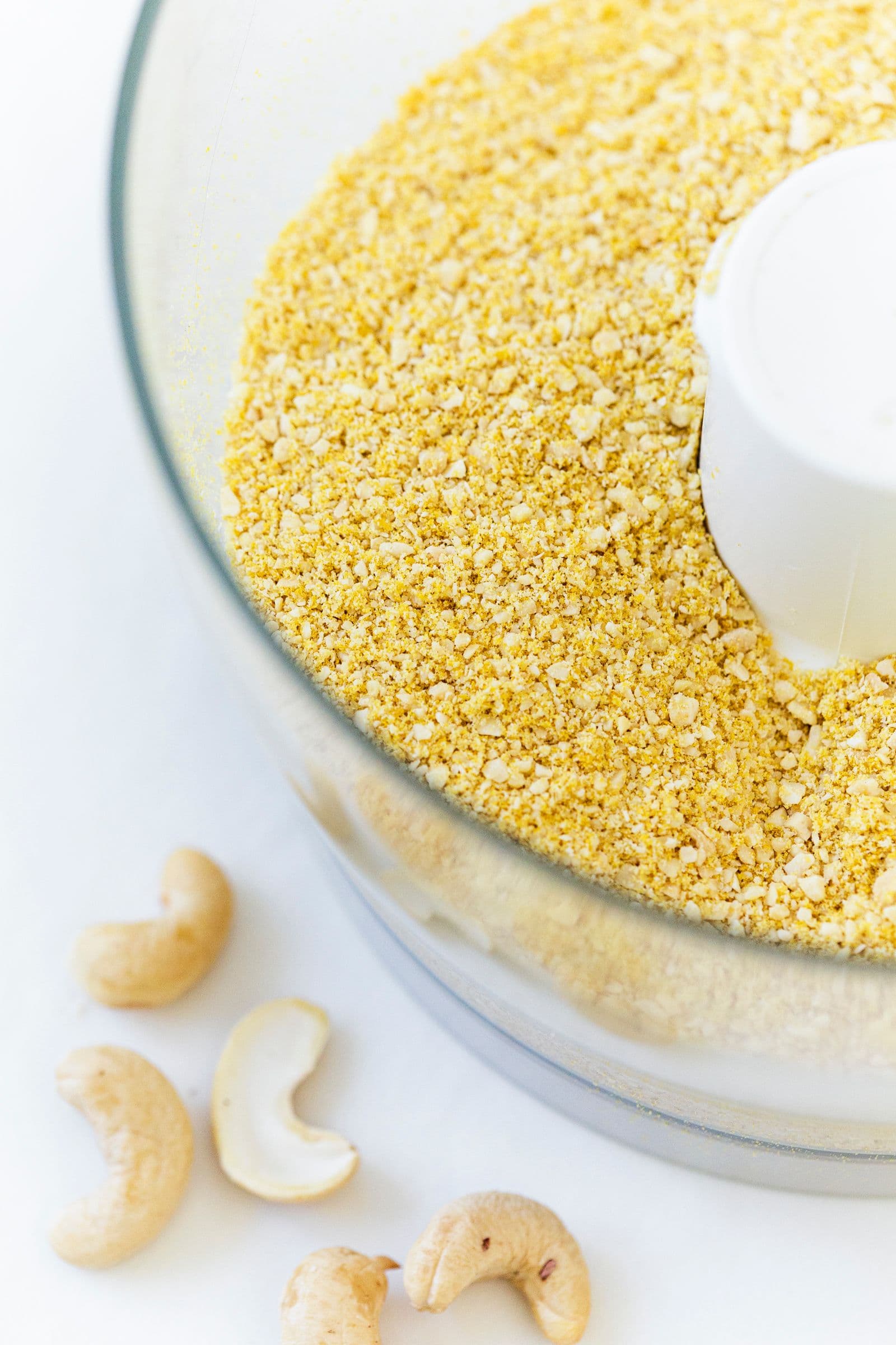 Vegan parmesan cheese being pulsed in a food processor with cashews on the side.
