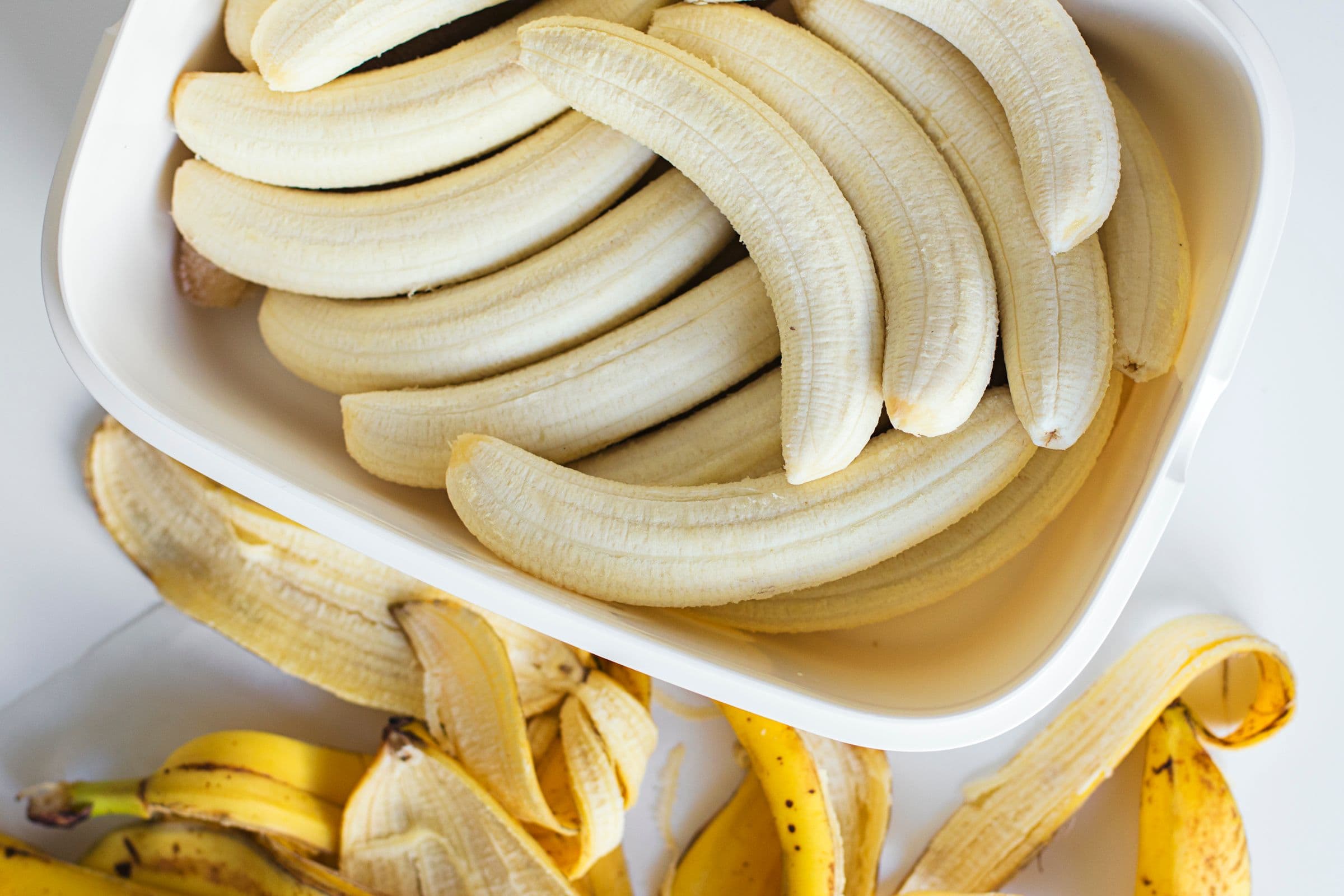 Bananas maduras numa caixa branca, com as cascas espalhadas à volta.