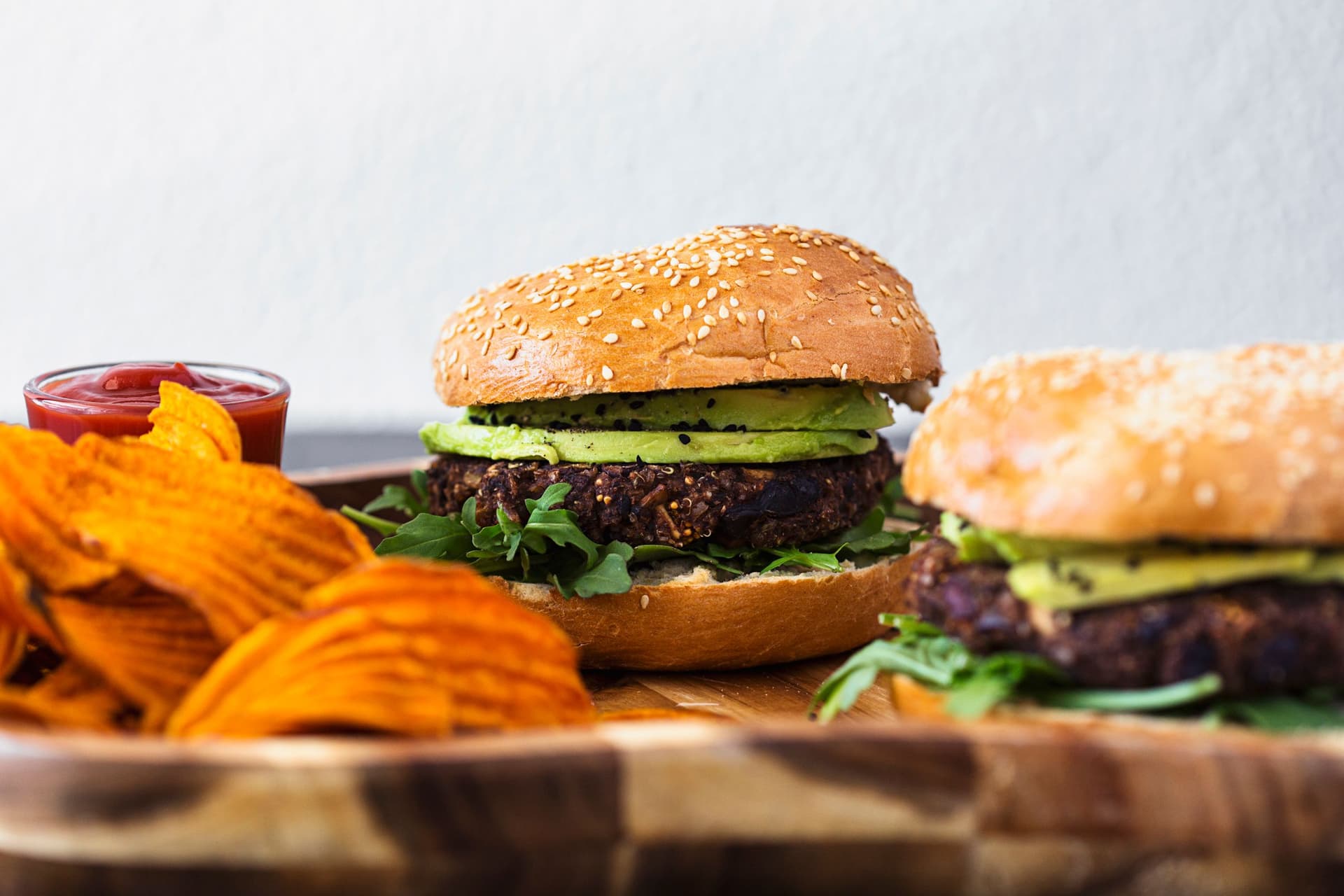 Vegan black bean burger with lettuce and sweet potato chips served on a wooden plate.