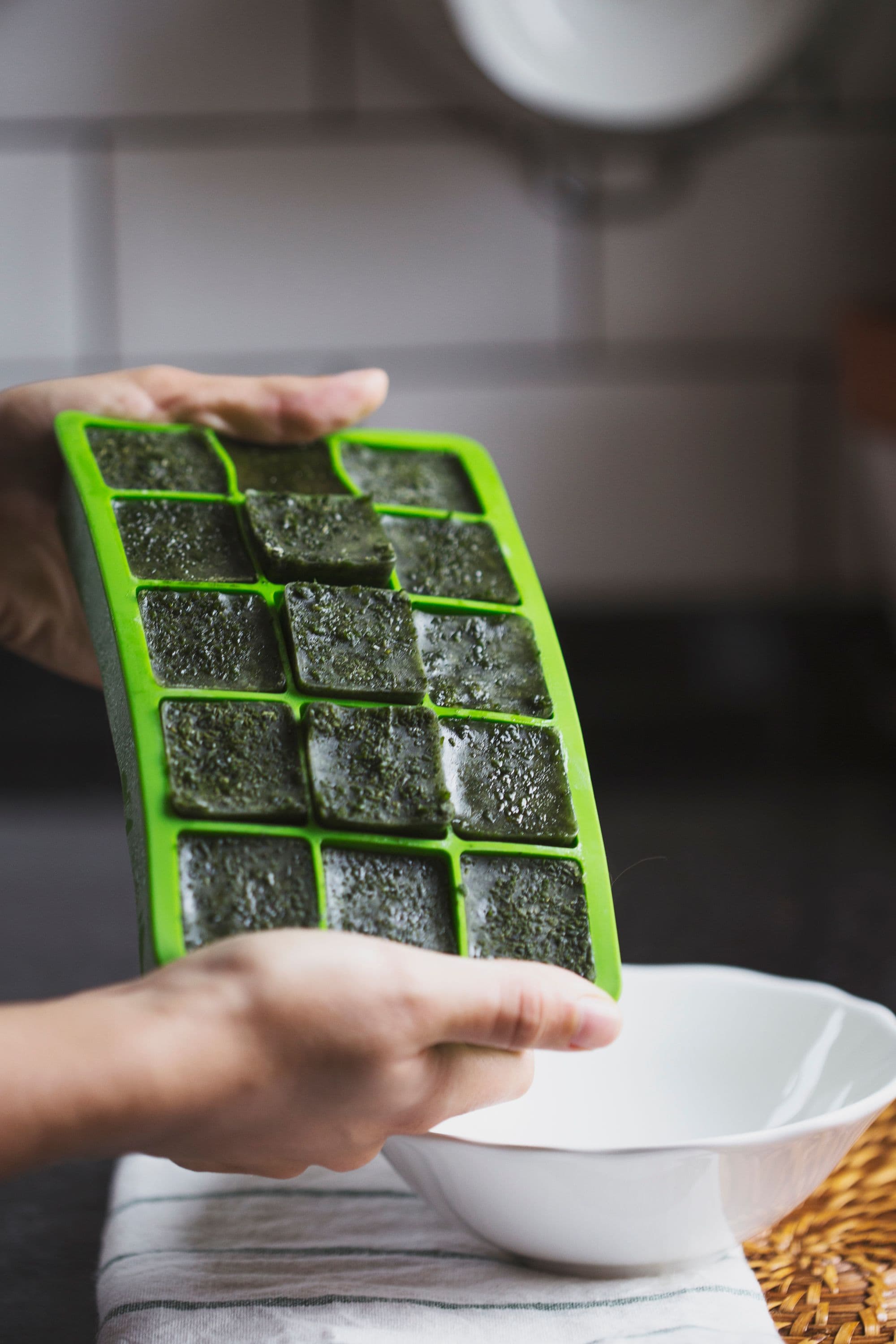 Hands pressing green cubes out of the silicone tray into a white bowl.
