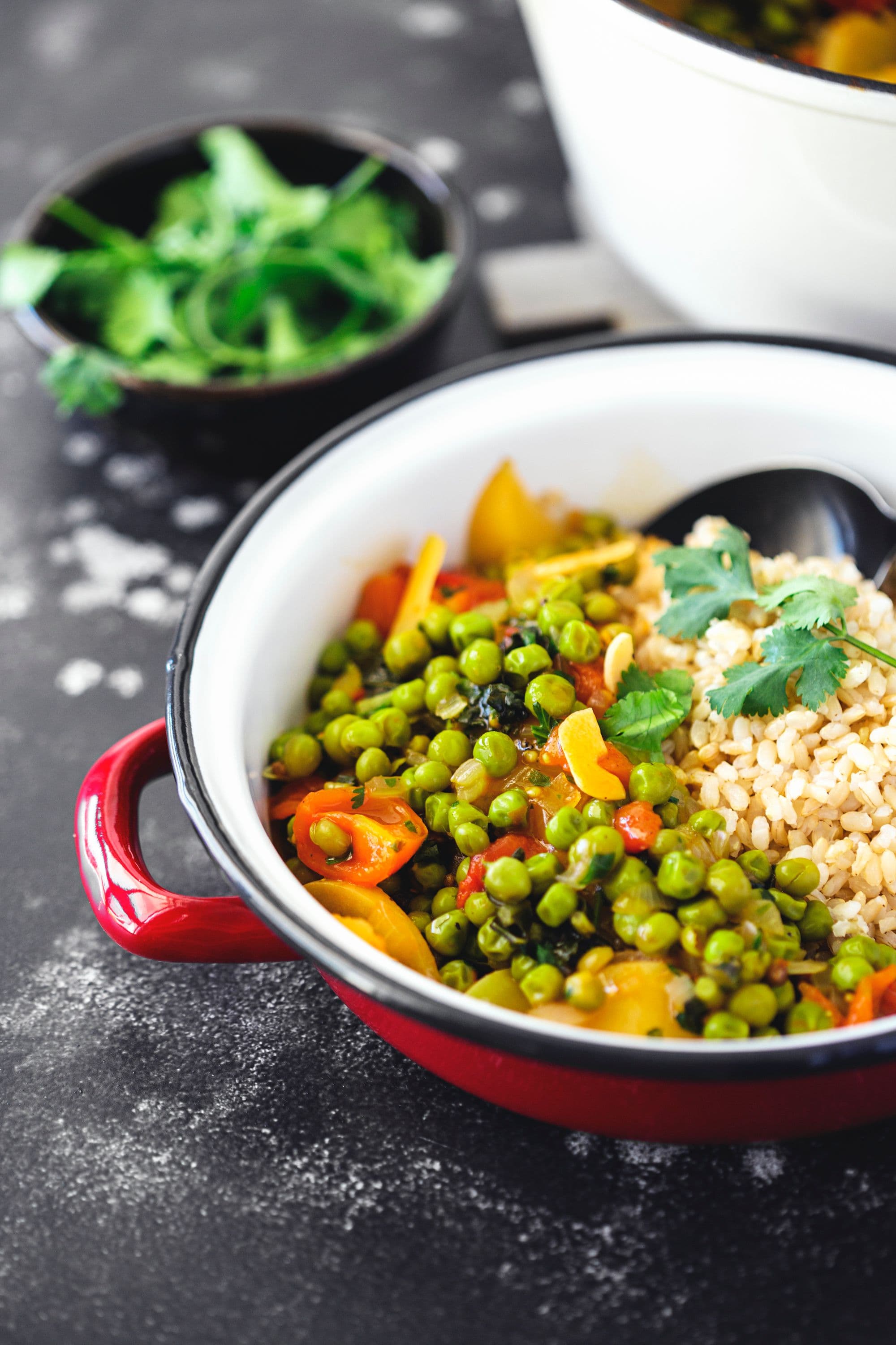 Rustic-style shallow pot with rice and pea stew, placed on a dark textured surface.