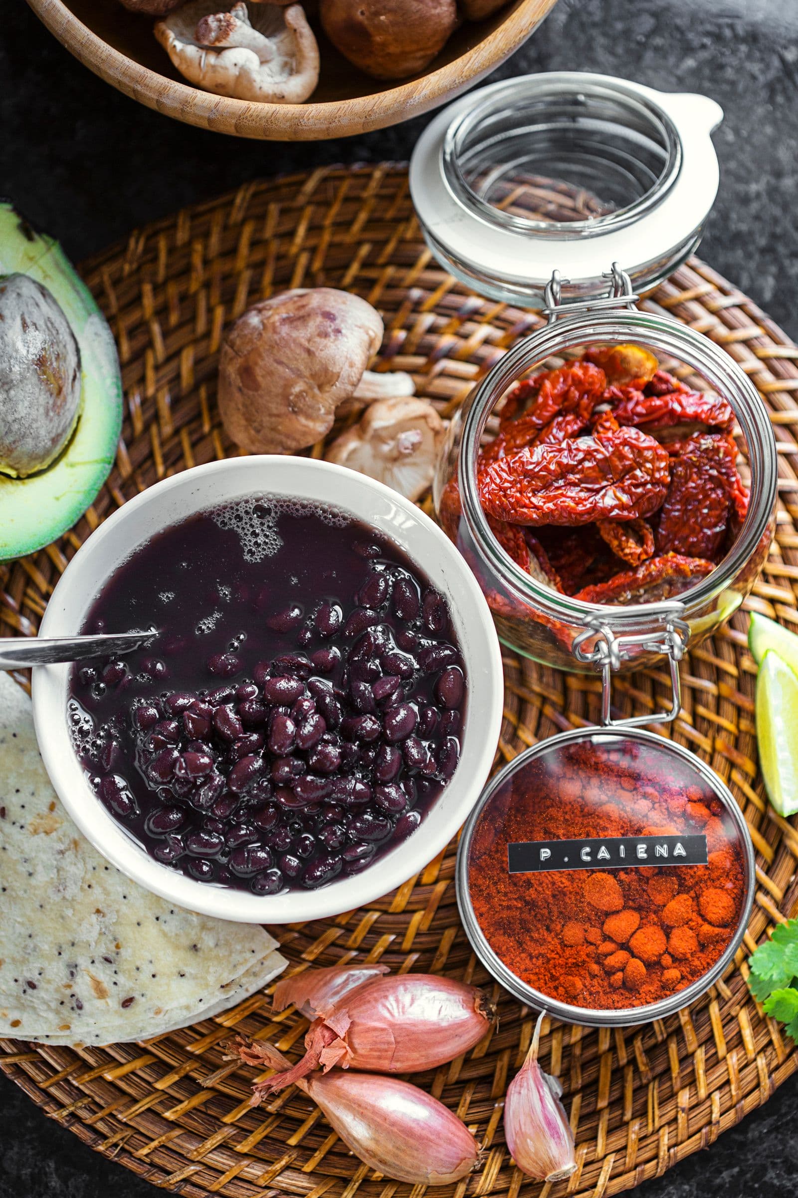 Vista de cima dos ingredientes da receita: feijão preto, cogumelos, abacate, chalotas, especiarias e lima.