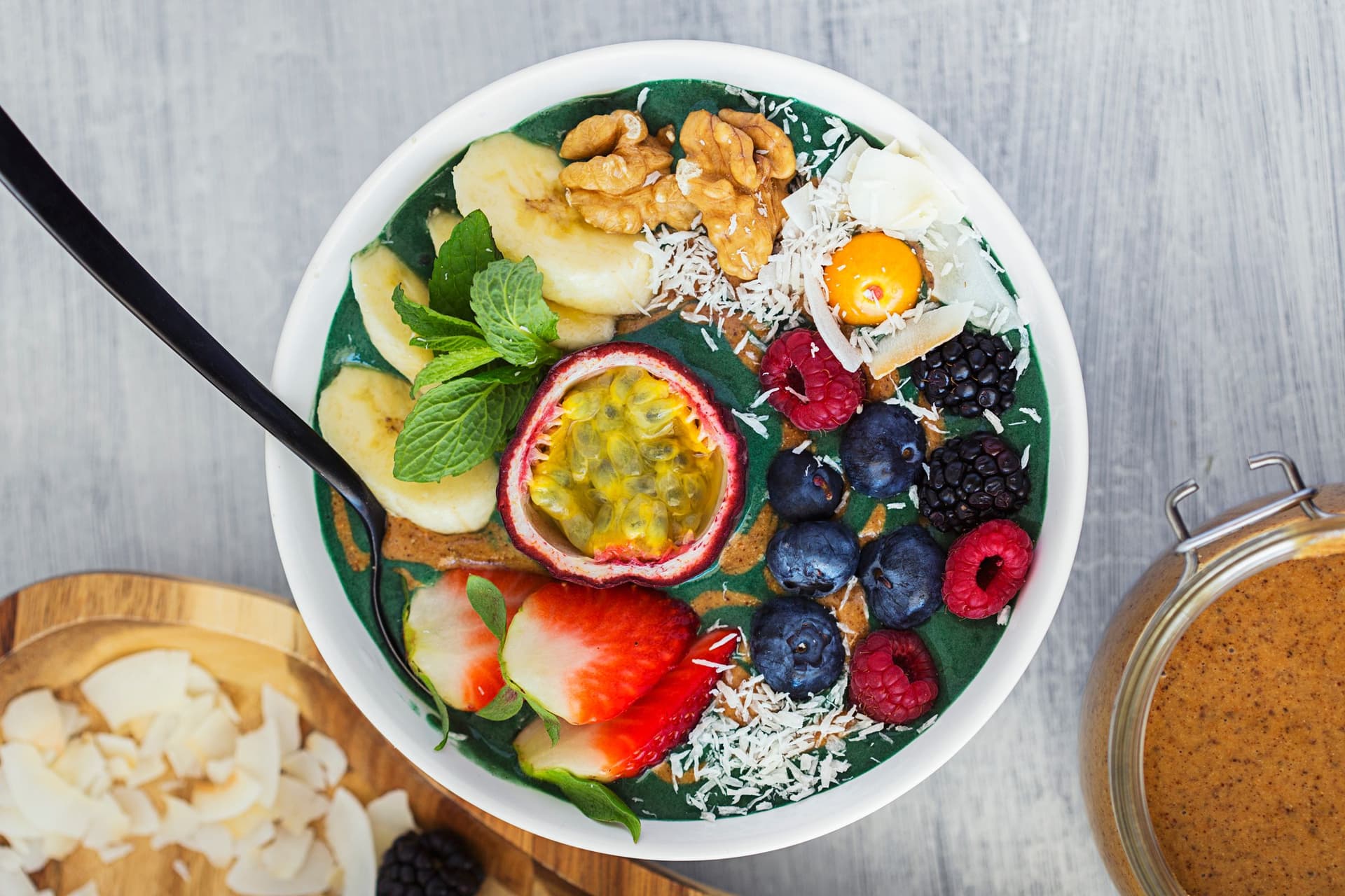 Taça de nicecream de banana e spirulina com maracujá, coco ralado, nozes e frutos vermelhos frescos.