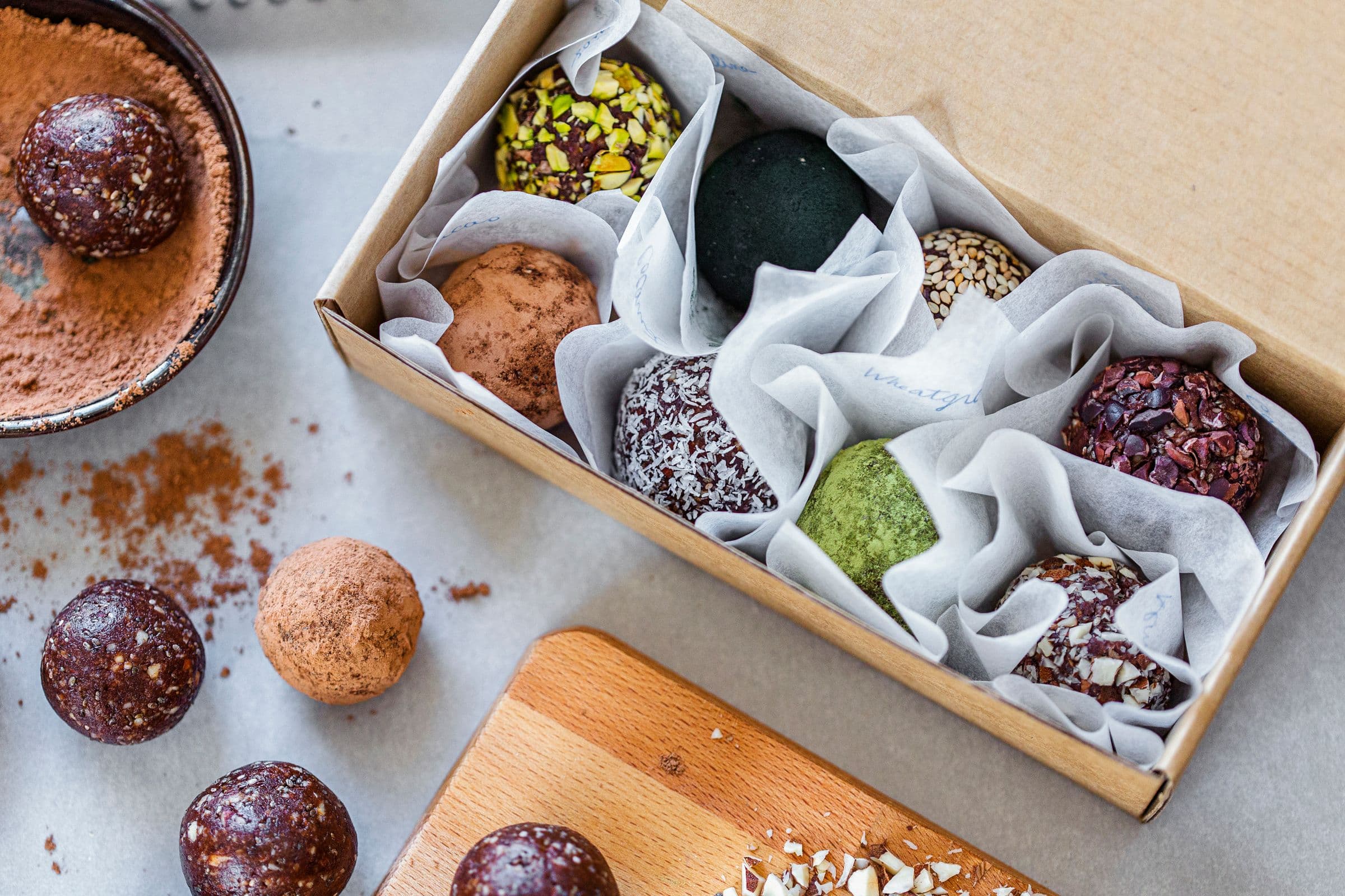 Gift box filled with cacao and almond energy balls rolled in various toppings like seeds, pistachio, and cocoa.