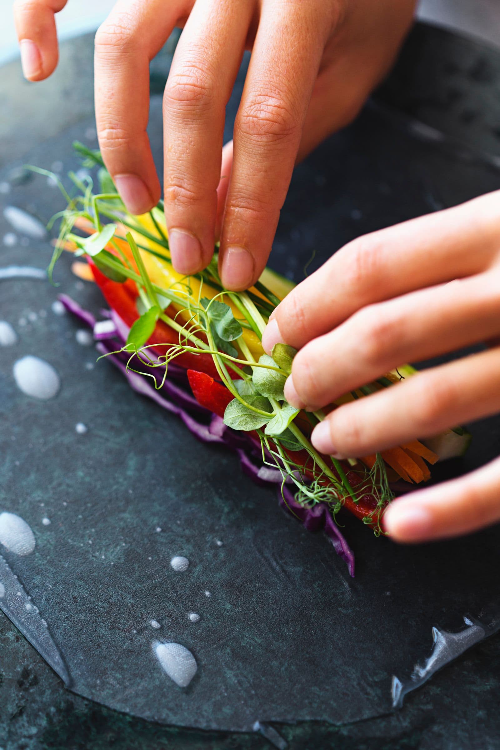 Close-up of hands placing colourful veggies onto rice paper.