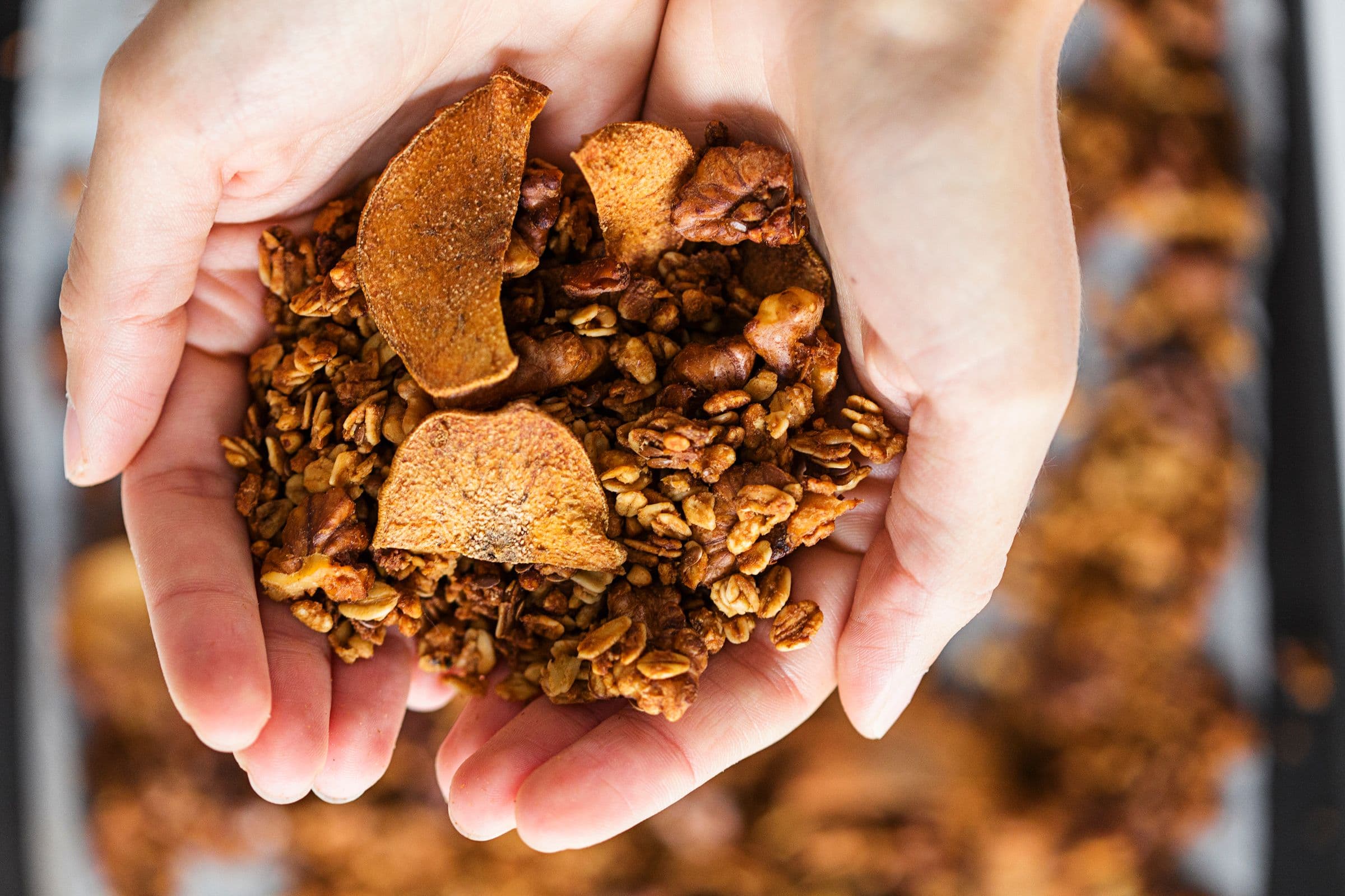 Two hands holding a portion of pear and ginger granola.