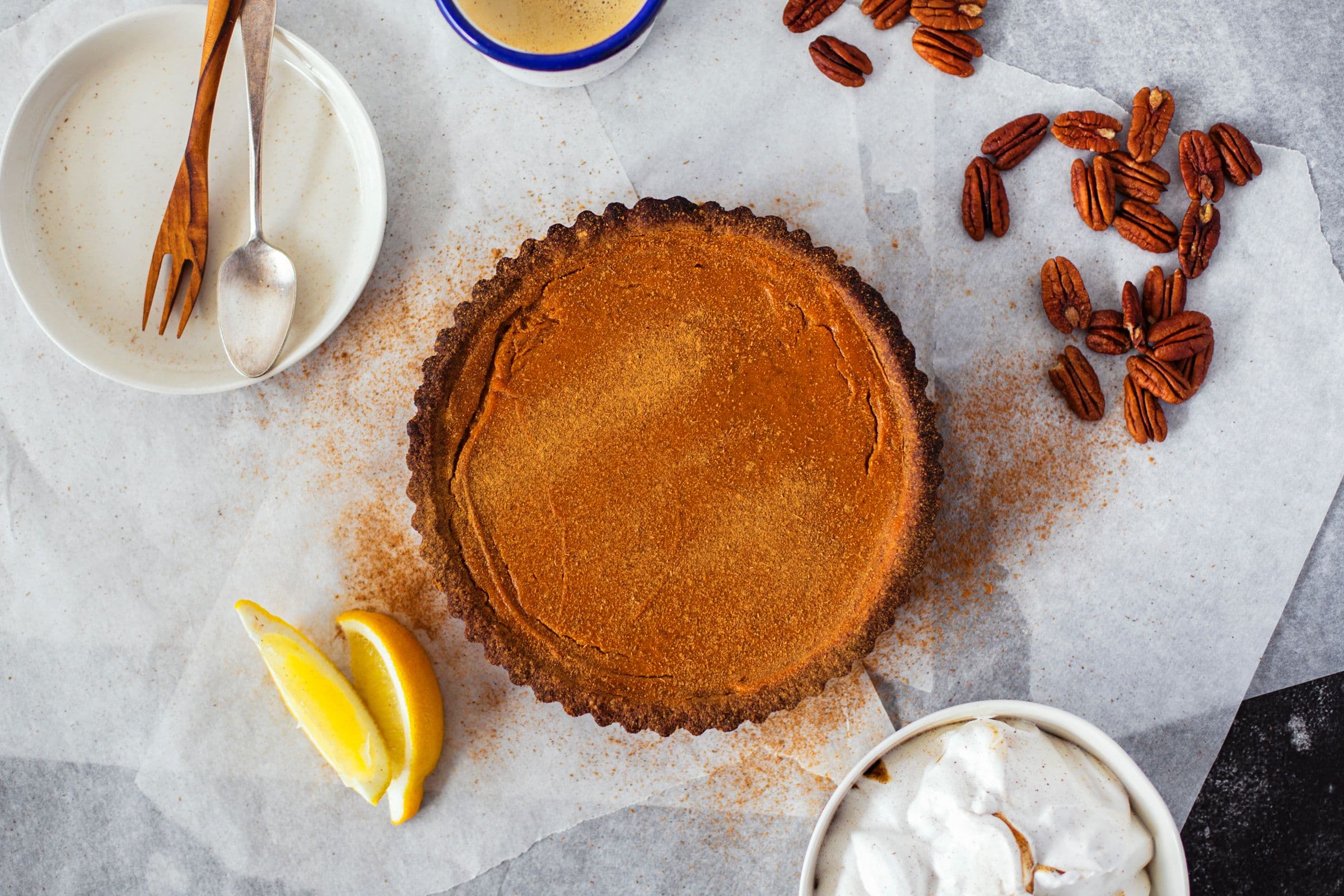 Tarte de batata-doce com citrinos sobre papel vegetal, decorada com gomo de limão, nozes pecan e uma taça de chantilly.