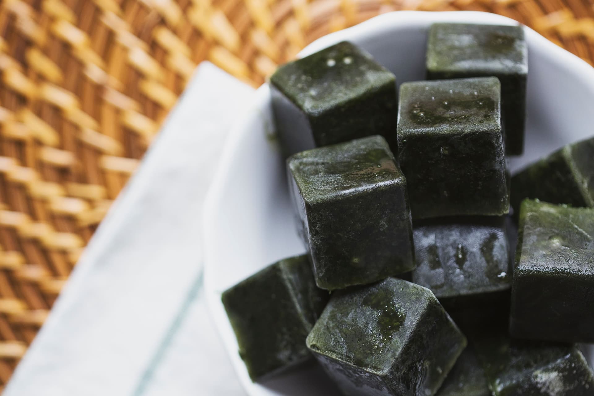 Pile of frozen green cubes stacked inside a white bowl on a textured surface.
