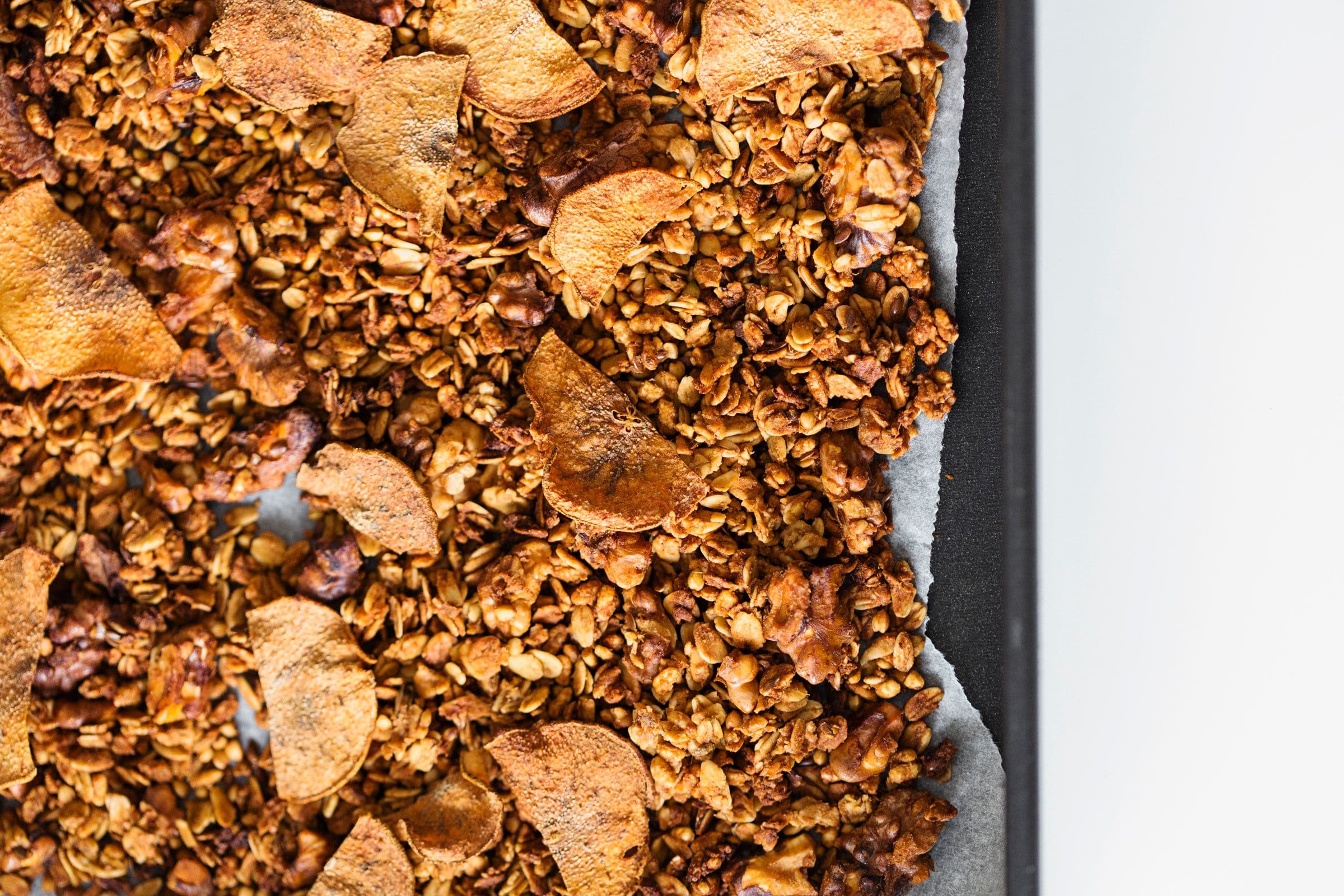 Close-up of dried pear slices over a tray of granola on a white background.