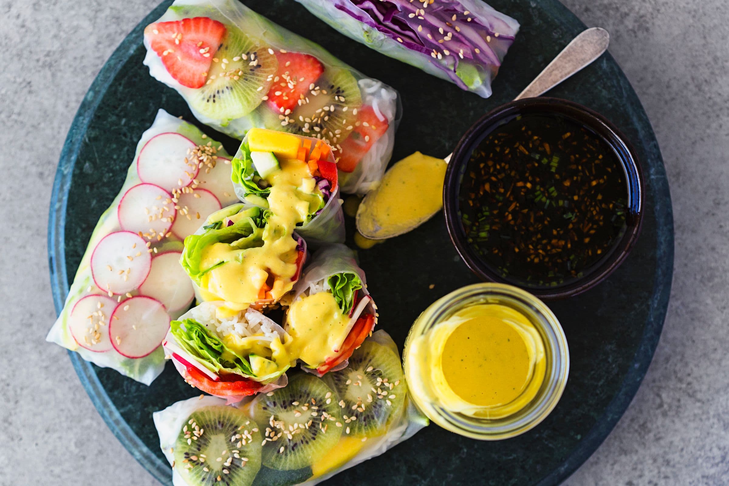 Colourful rainbow spring rolls served with two dipping sauces on a dark platter.