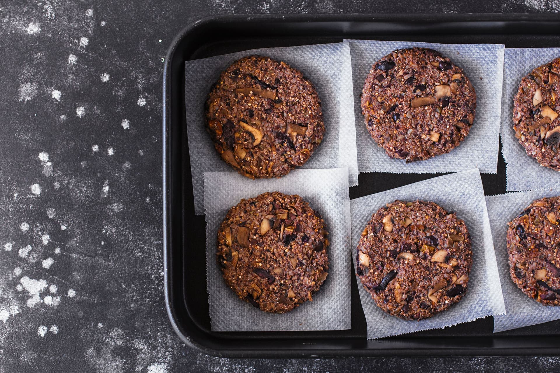 Uncooked burger patties neatly arranged on a parchment-lined tray.