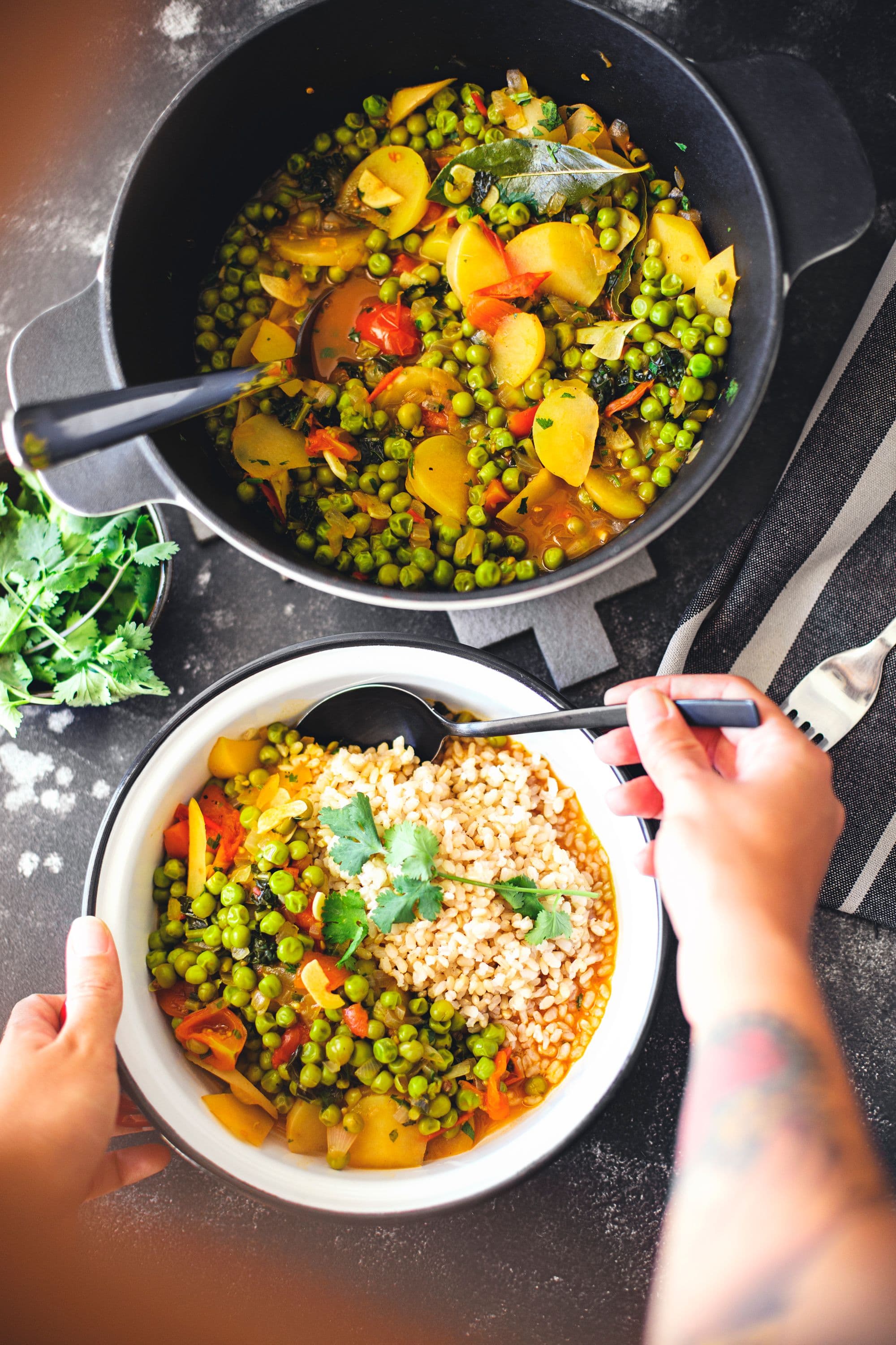 Hands spooning vegan pea stew from a black pot into a white bowl of rice.