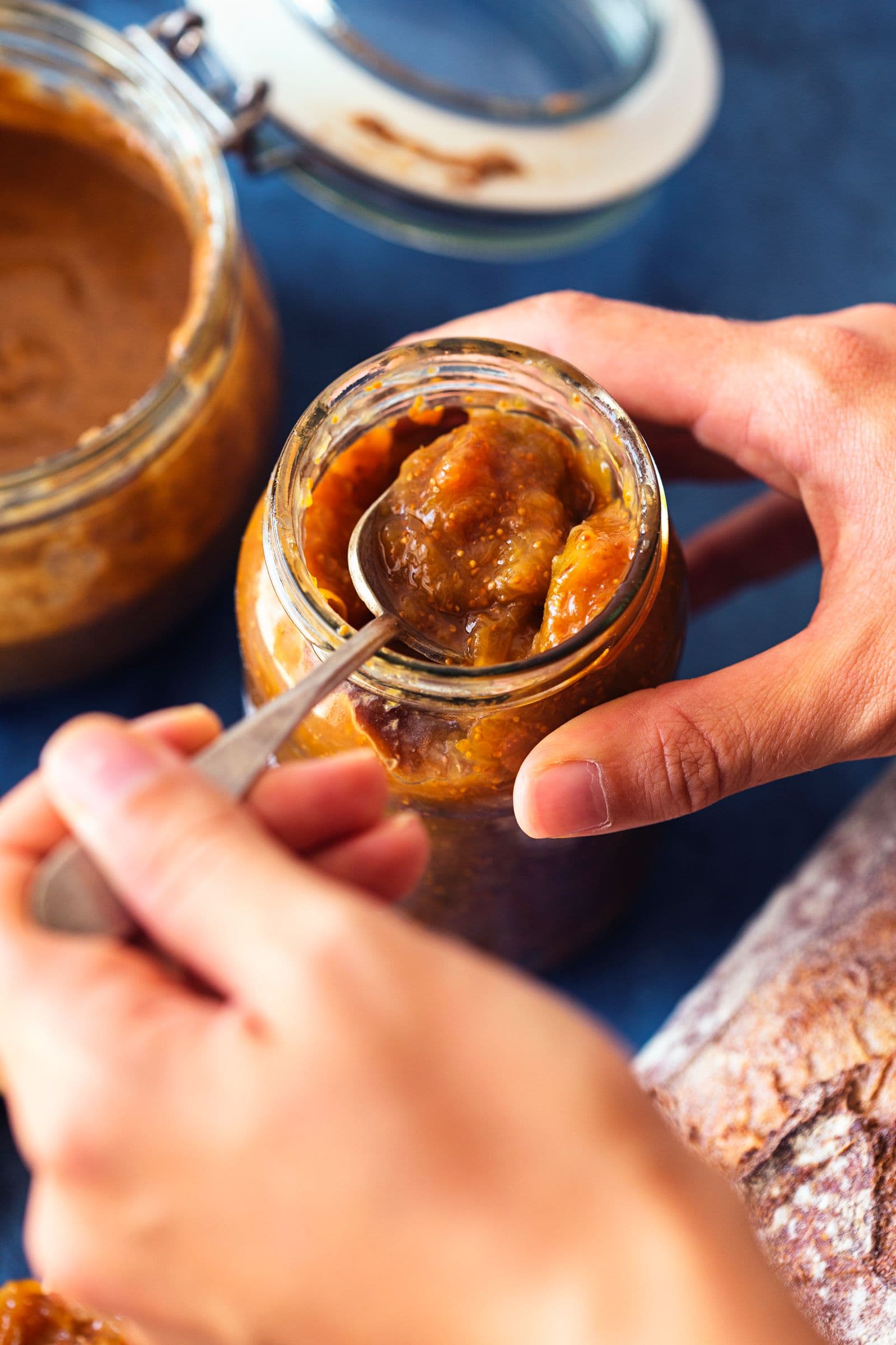 Close-up of a handing dipping a spoon into thick fig and ginger jam.
