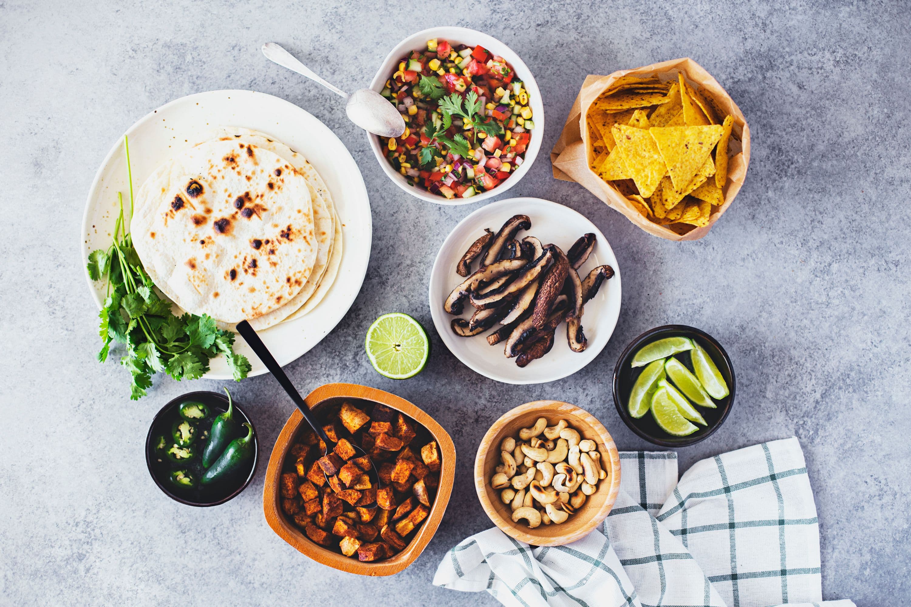 Flatlay of bowls with grilled mushrooms, salsa, nachos, lime wedges and tortillas.