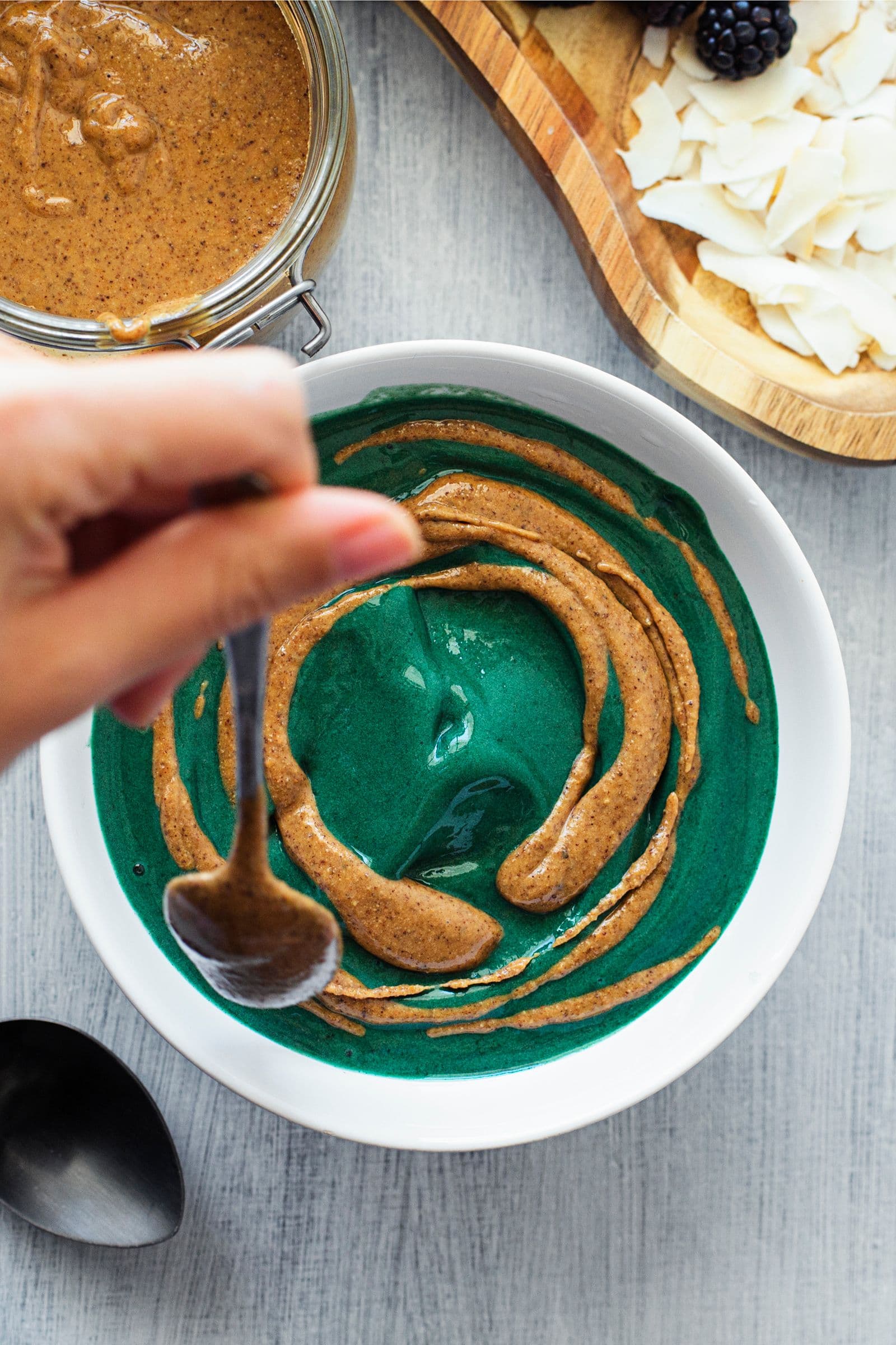 Swirling peanut butter into spirulina nicecream in a white bowl.