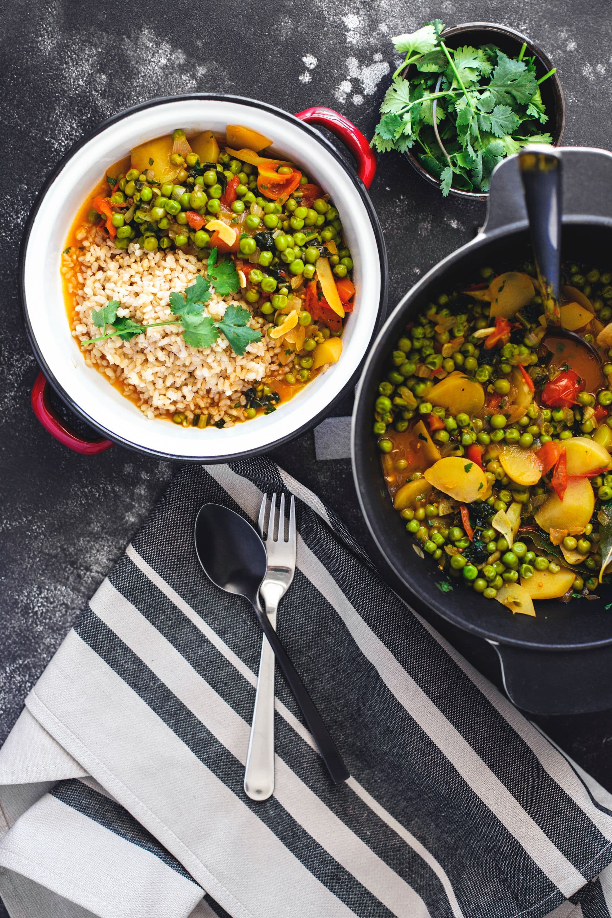 Overhead shot of a bowl filled with pea stew and a pot with rice and stew, on a striped tablecloth.
