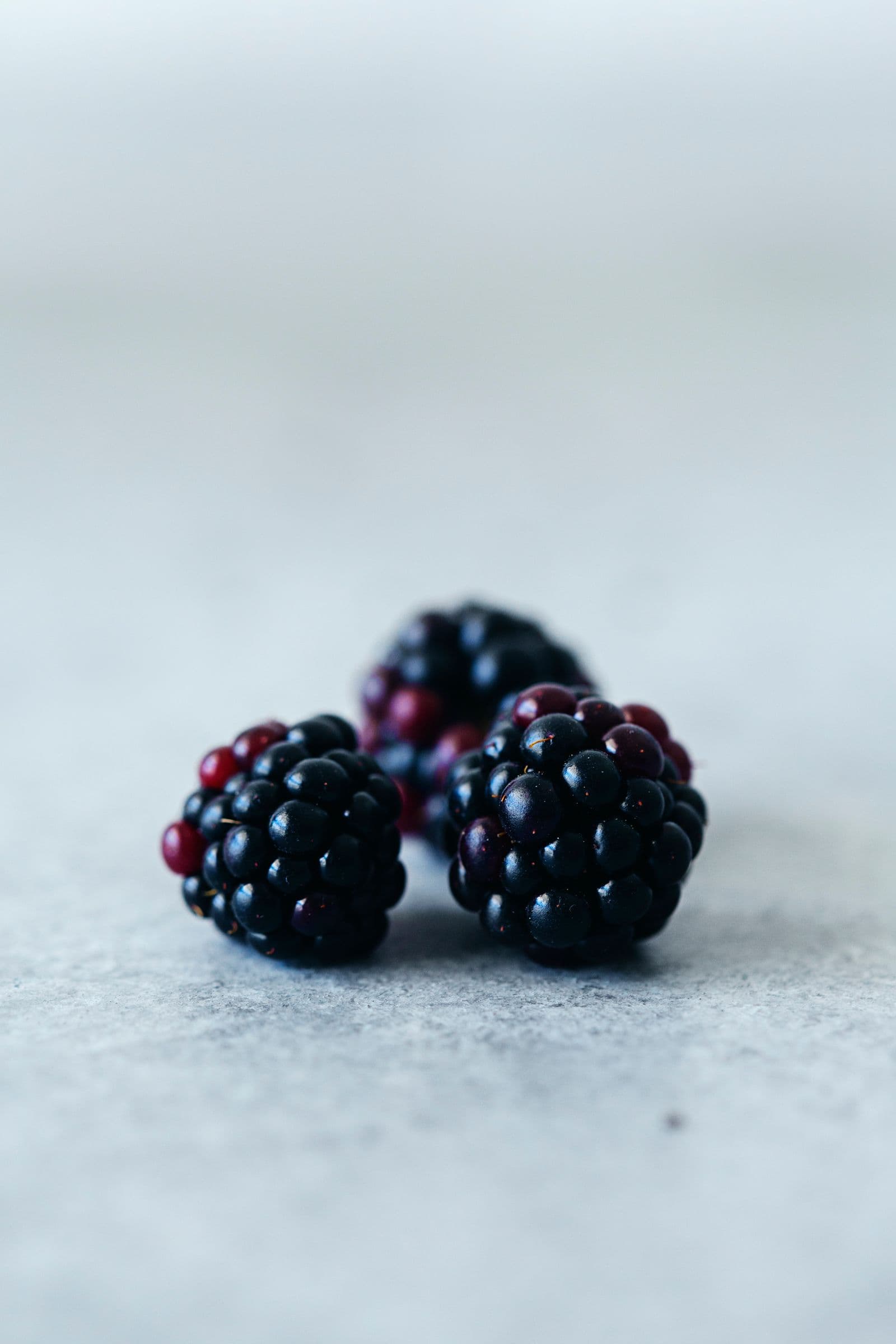 Macro shot of three fresh blackberries on a white surface.