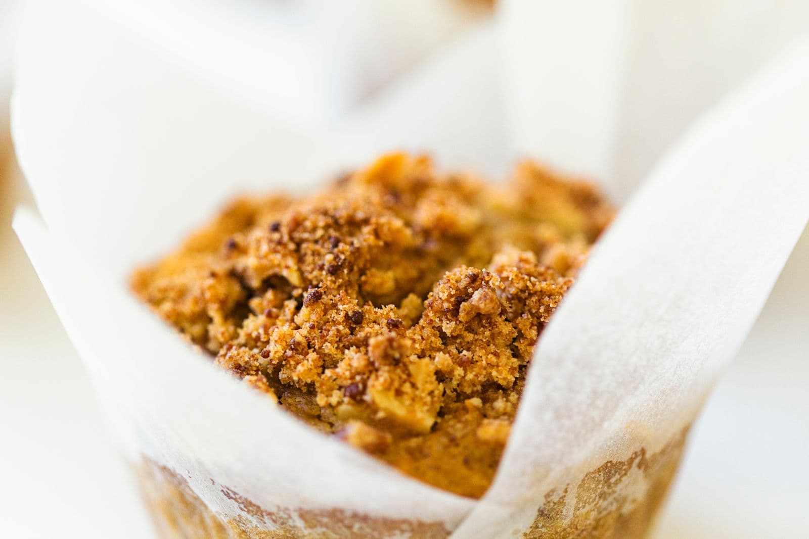 Close-up of a golden-brown muffin with crumbly topping in a parchment paper liner.