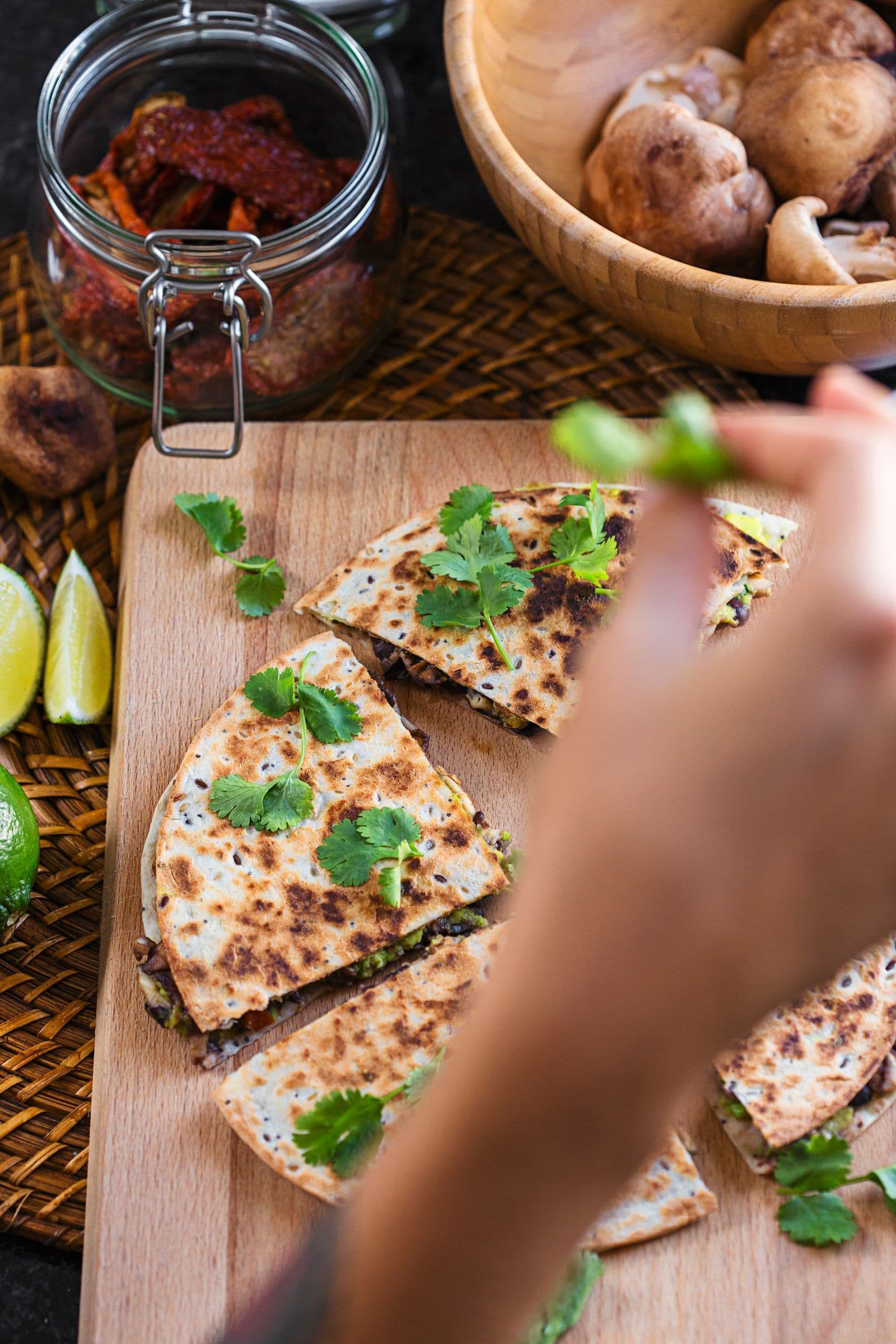 Mão a decorar quesadillas já prontas com coentros frescos sobre uma tábua de madeira.