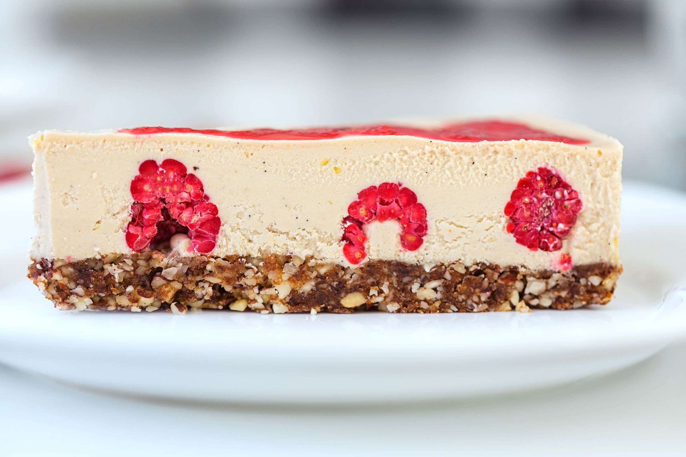 Fatia de cheesecake vista de lado, com framboesas inteiras visíveis no interior.