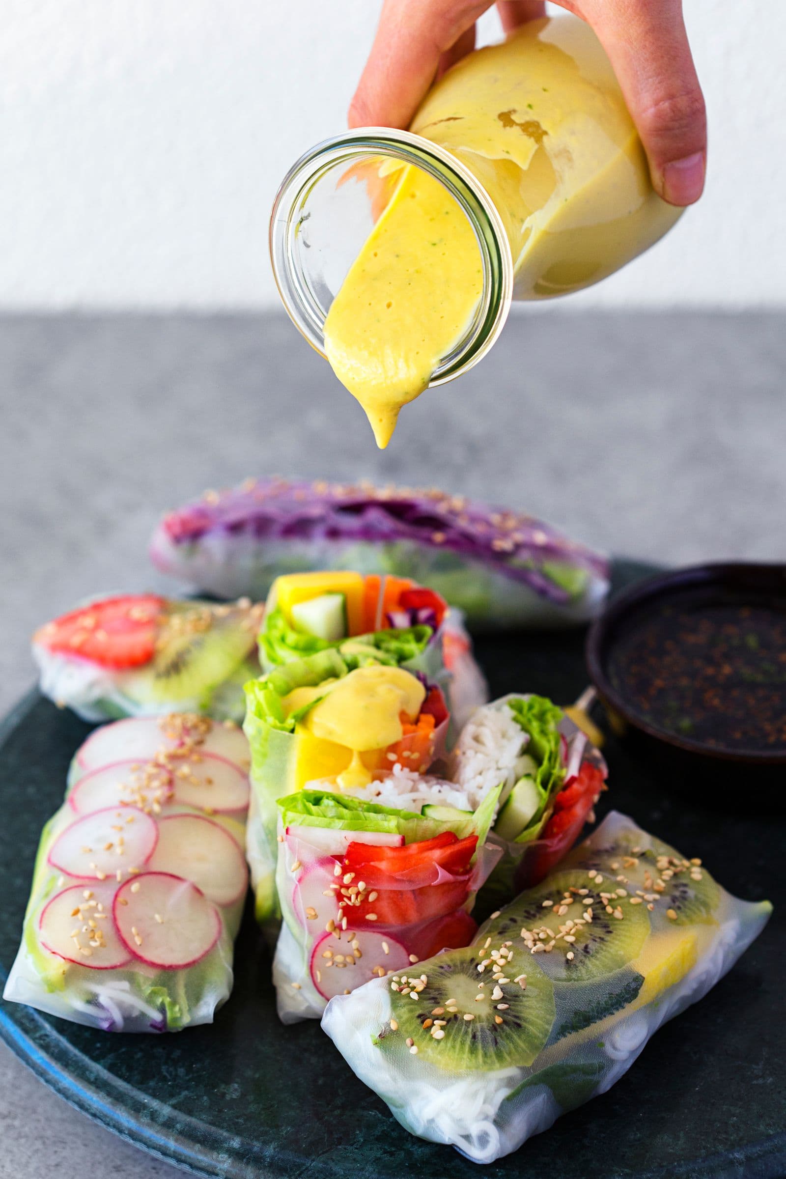 Hand pouring yellow dipping sauce over spring rolls.