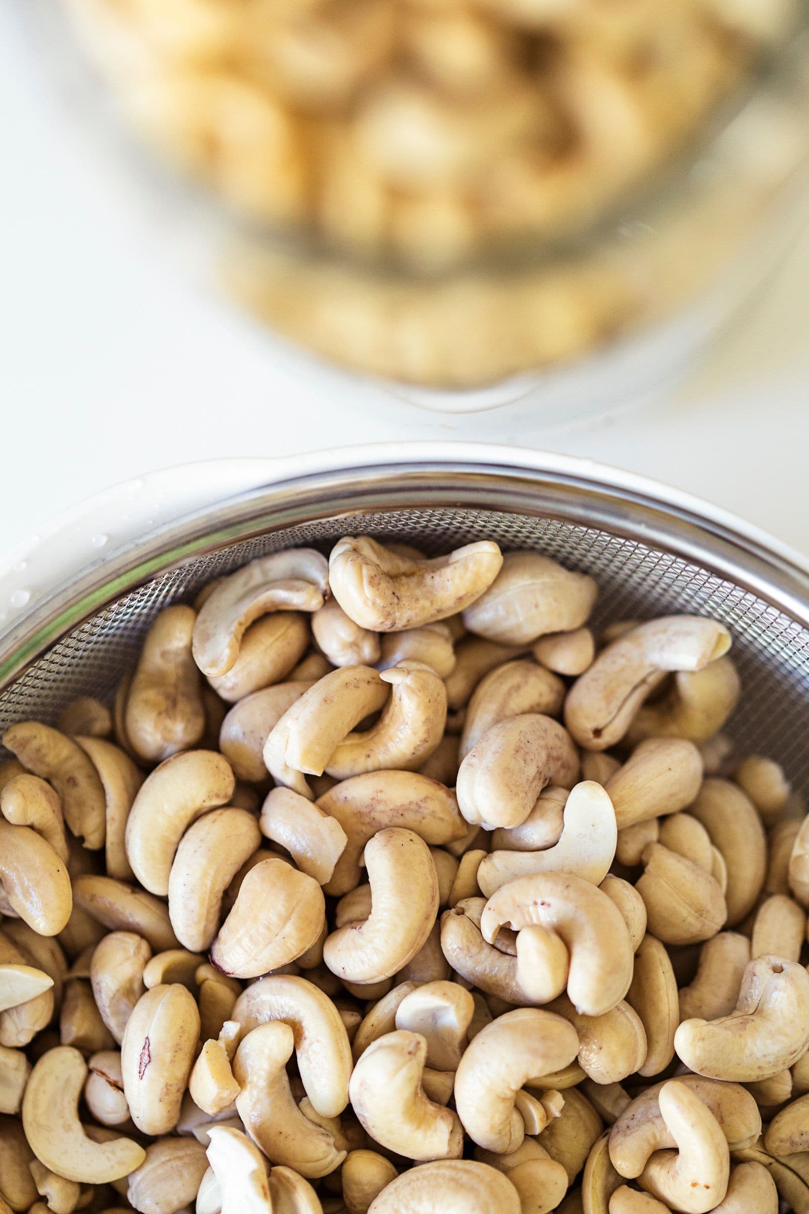 Close-up of soaked cashew nuts in a fine mesh strainer.