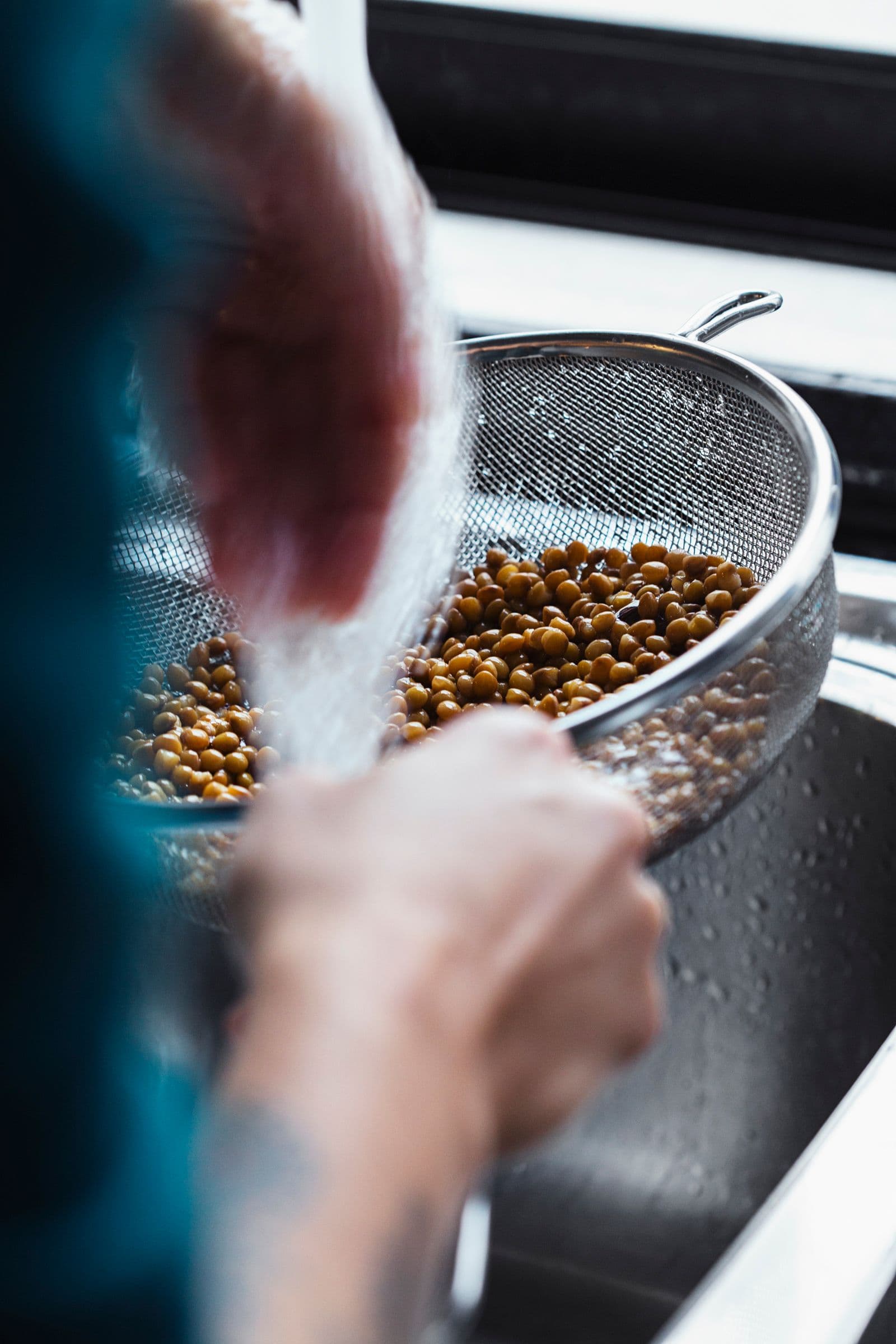 Lentils being rinsed in a sieve under running water before blending.