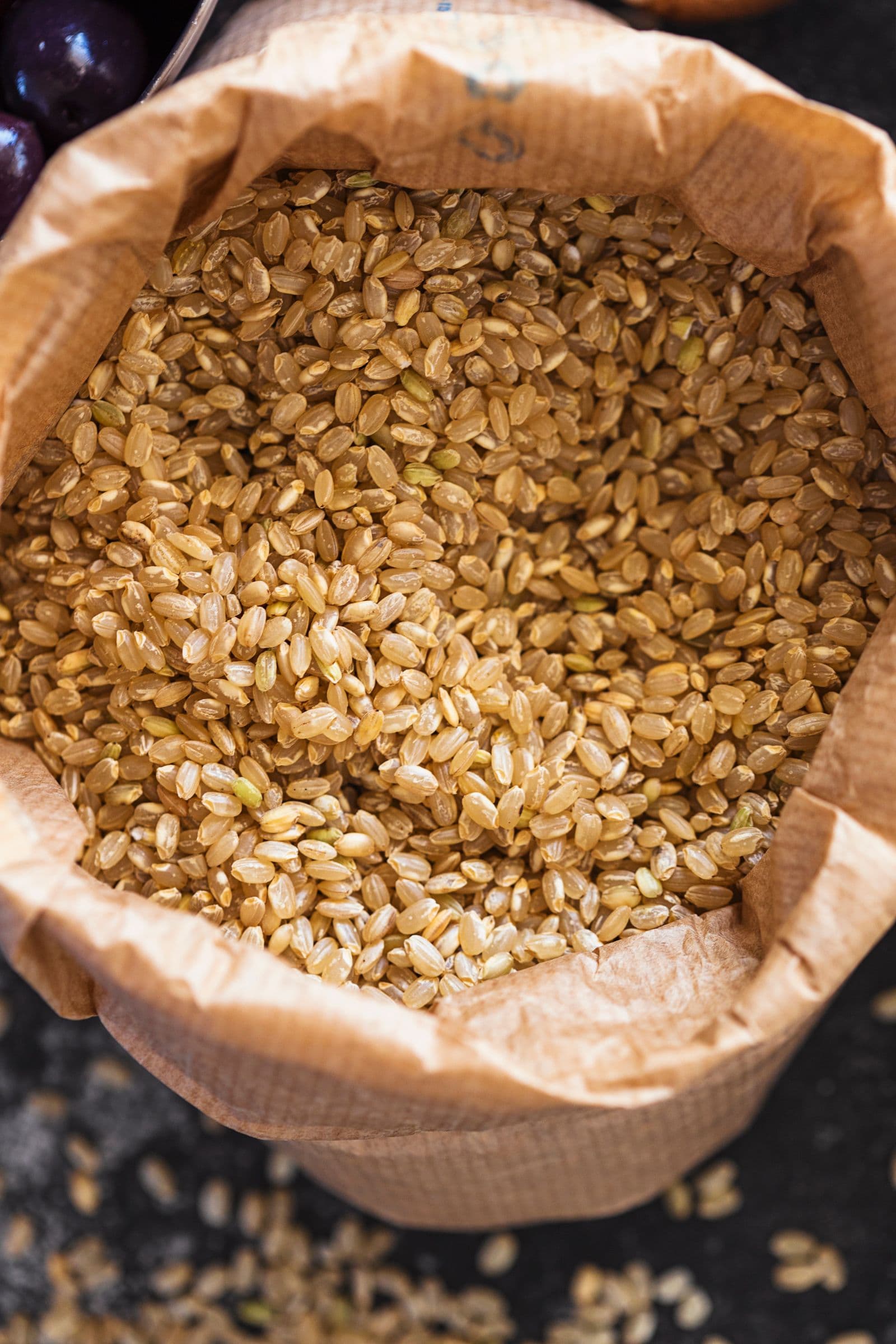 Rustic paper bag filled with brown rice on a dark background.