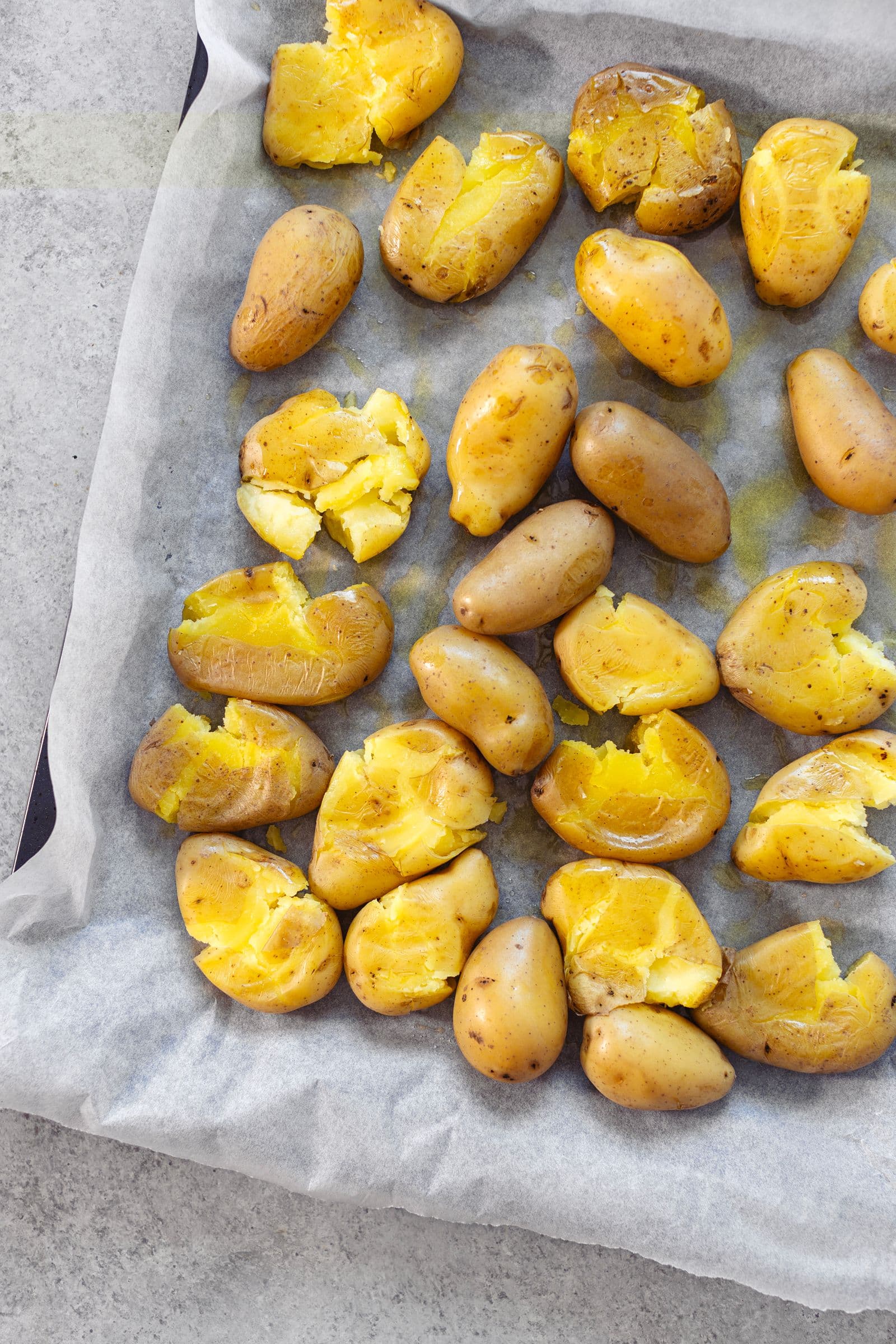 Batatas novas ligeiramente esmagadas e regadas com azeite, antes de irem ao forno