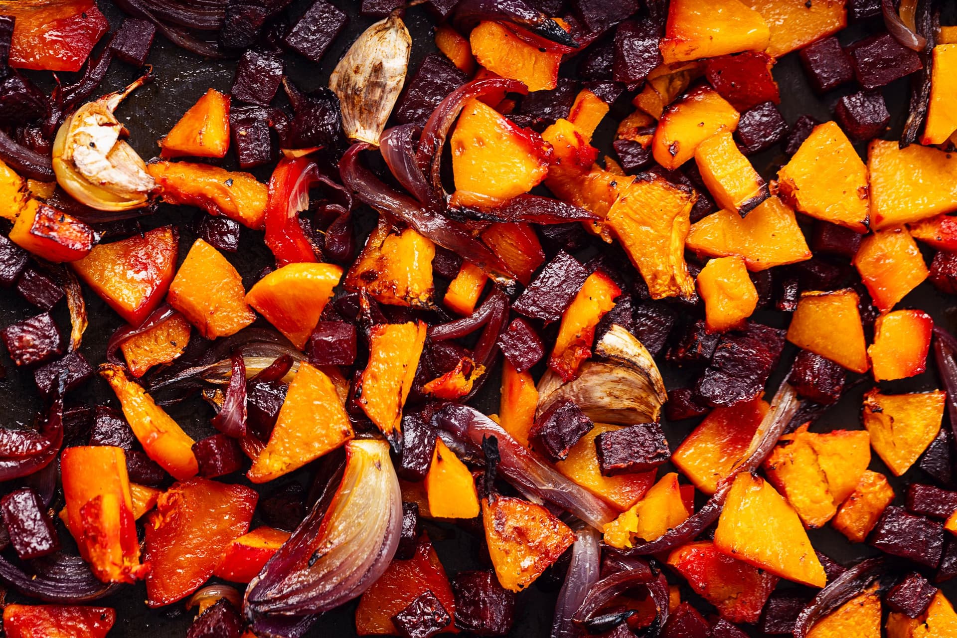 Close-up of roasted vegetables, including butternut squash, beetroot, red onion and garlic.