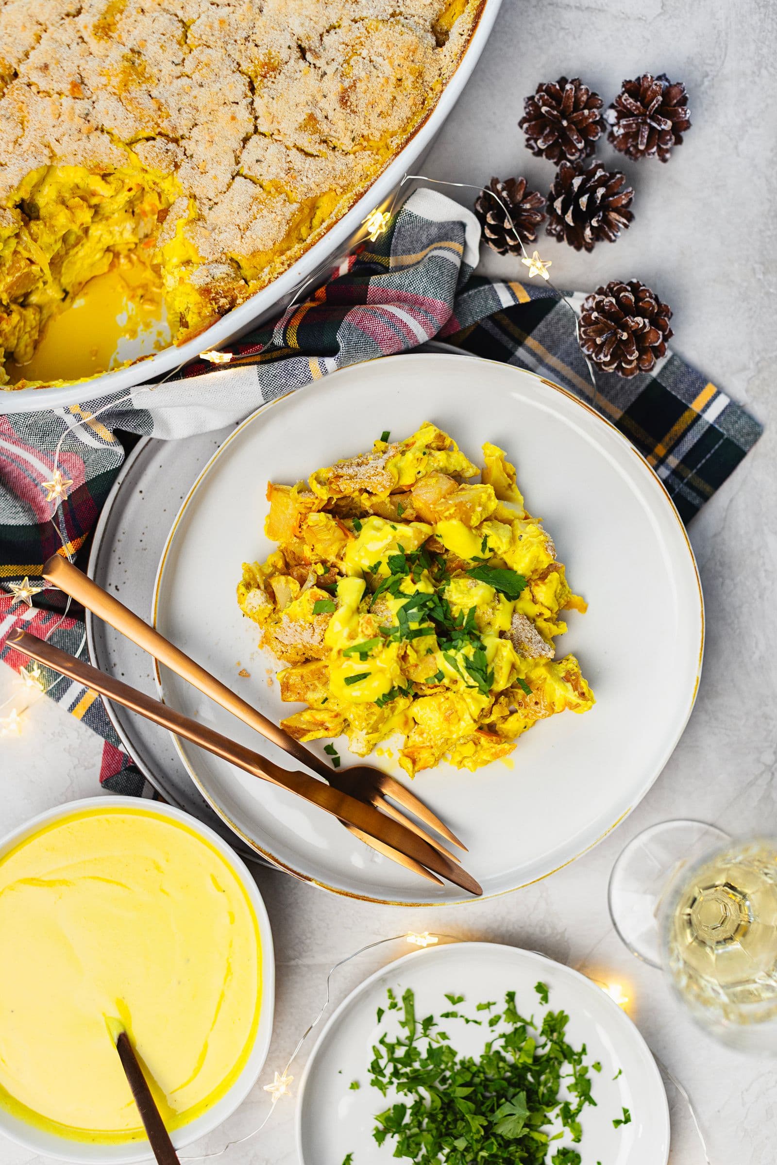 Prato com gratinado servido, talheres ao lado e a travessa grande em segundo plano.